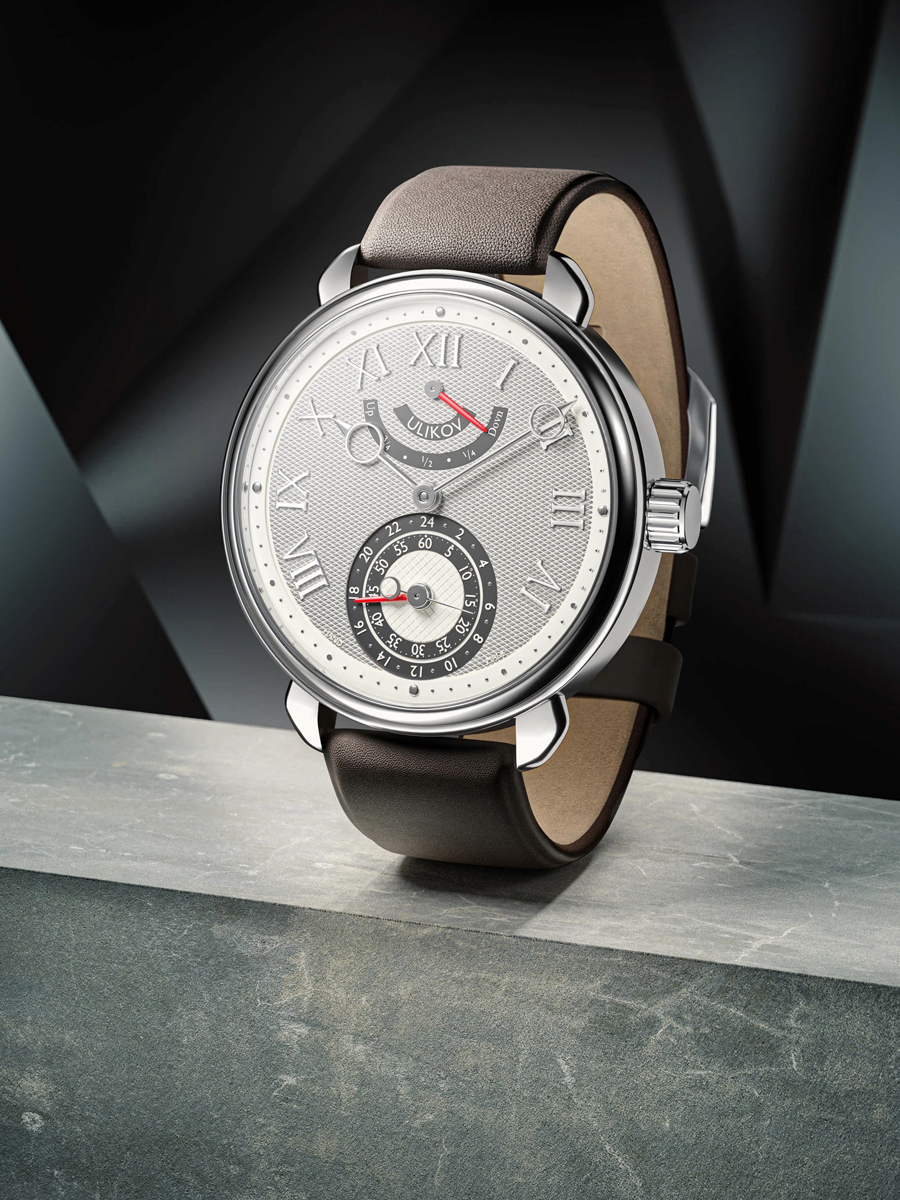 Orologio classico elegante marchio Ulikov con cassa argentata e cinturino in pelle marrone. Quadrante bianco lavorato a texture con numeri romani e complicazioni, appoggiato su superficie in pietra con sfondo geometrico scuro.