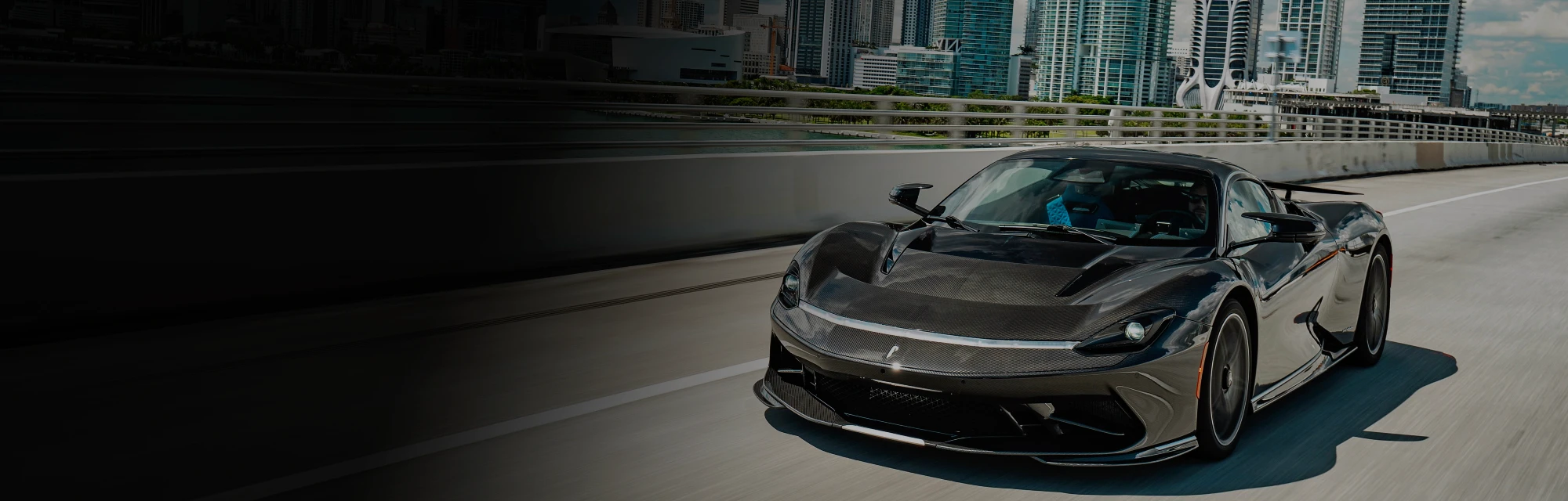 Black supercar driving across a Miami bridge with the city's skyline in the background, highlighting luxury and exotic car rentals available from Monarc VIP.