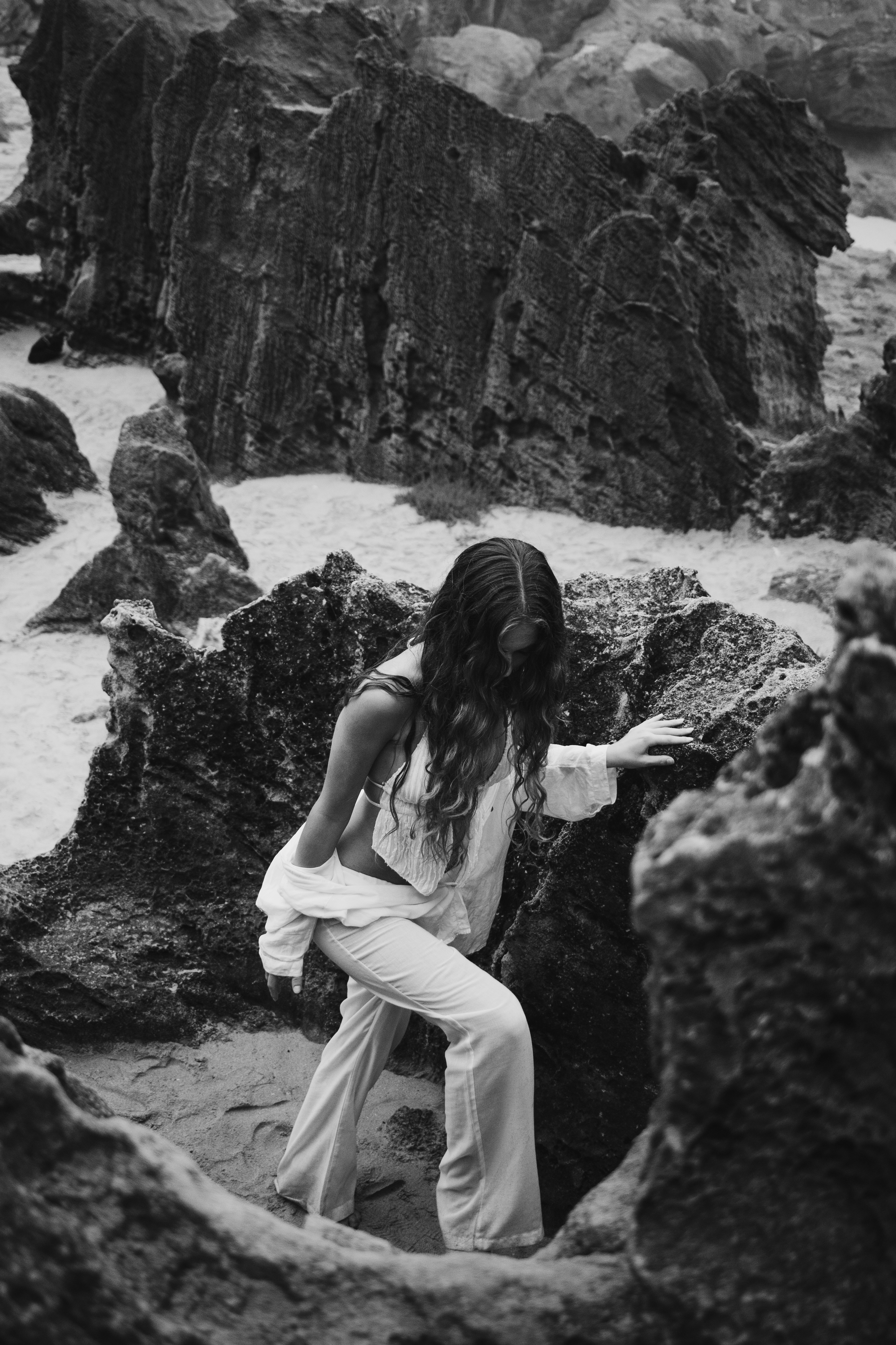 Woman in white clothing climbing rocky shore