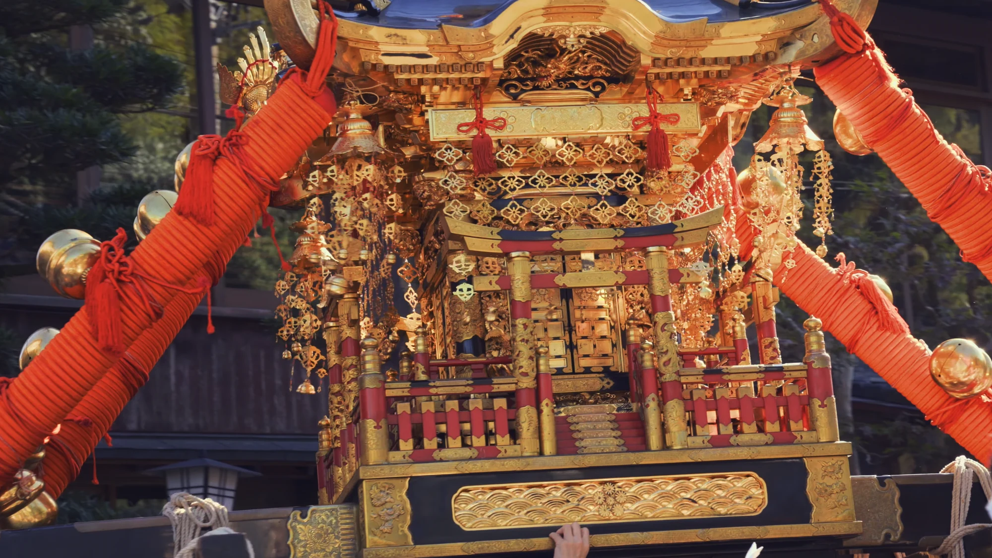 Gold lacquer and red rope detail on a Kinosaki festival float against the town roofline.