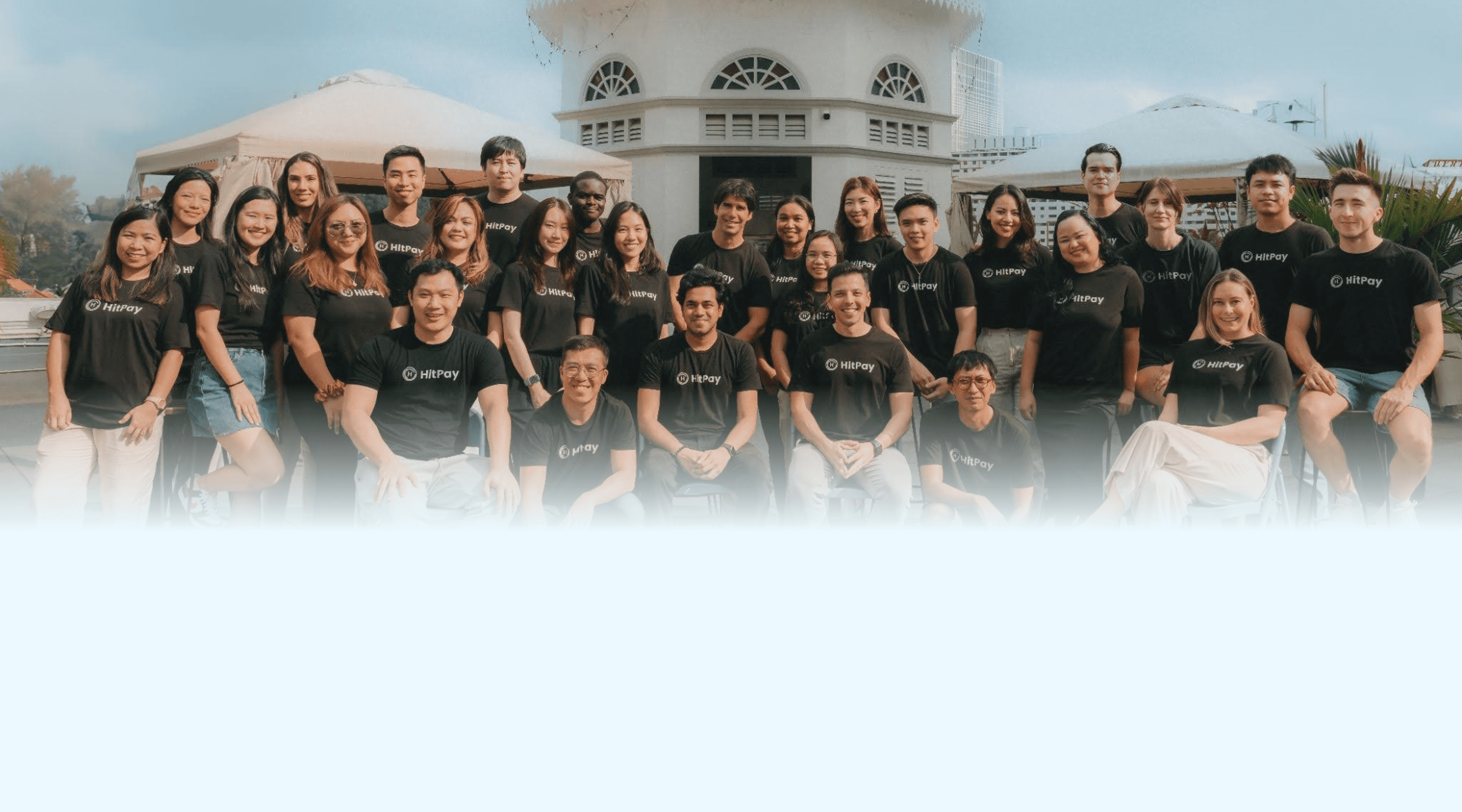 Group of people in "HitPay" shirts pose outdoors.