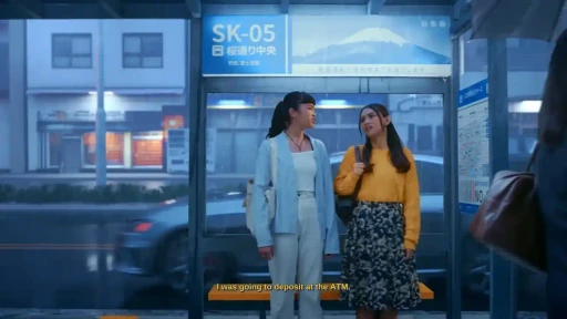 Two females at bus stop in Japan Tokyo rainy urban setting in cinematic commercial scene for DCOM Money Express, produced by Visual Producer Indonesia