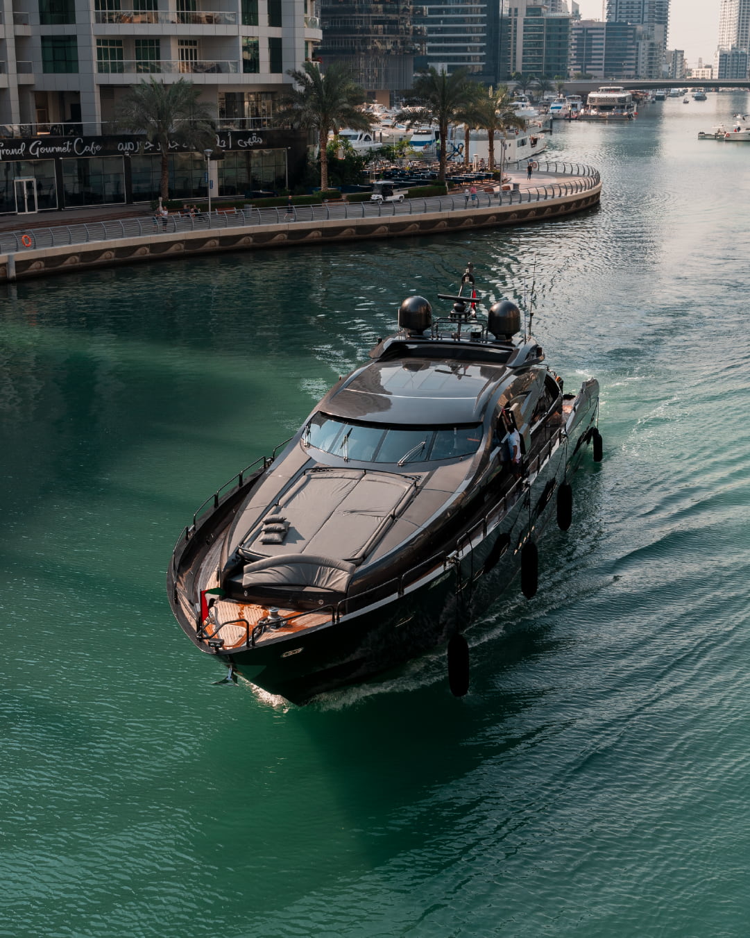 A black, luxury yacht cruising through the clear waters of Dubai Marina.
