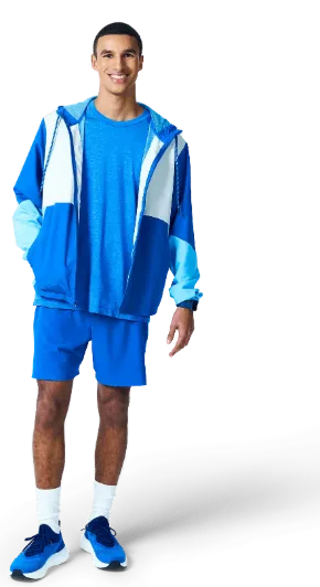 A person stands confidently in athletic attire, featuring a blue shirt, shorts, and sneakers.