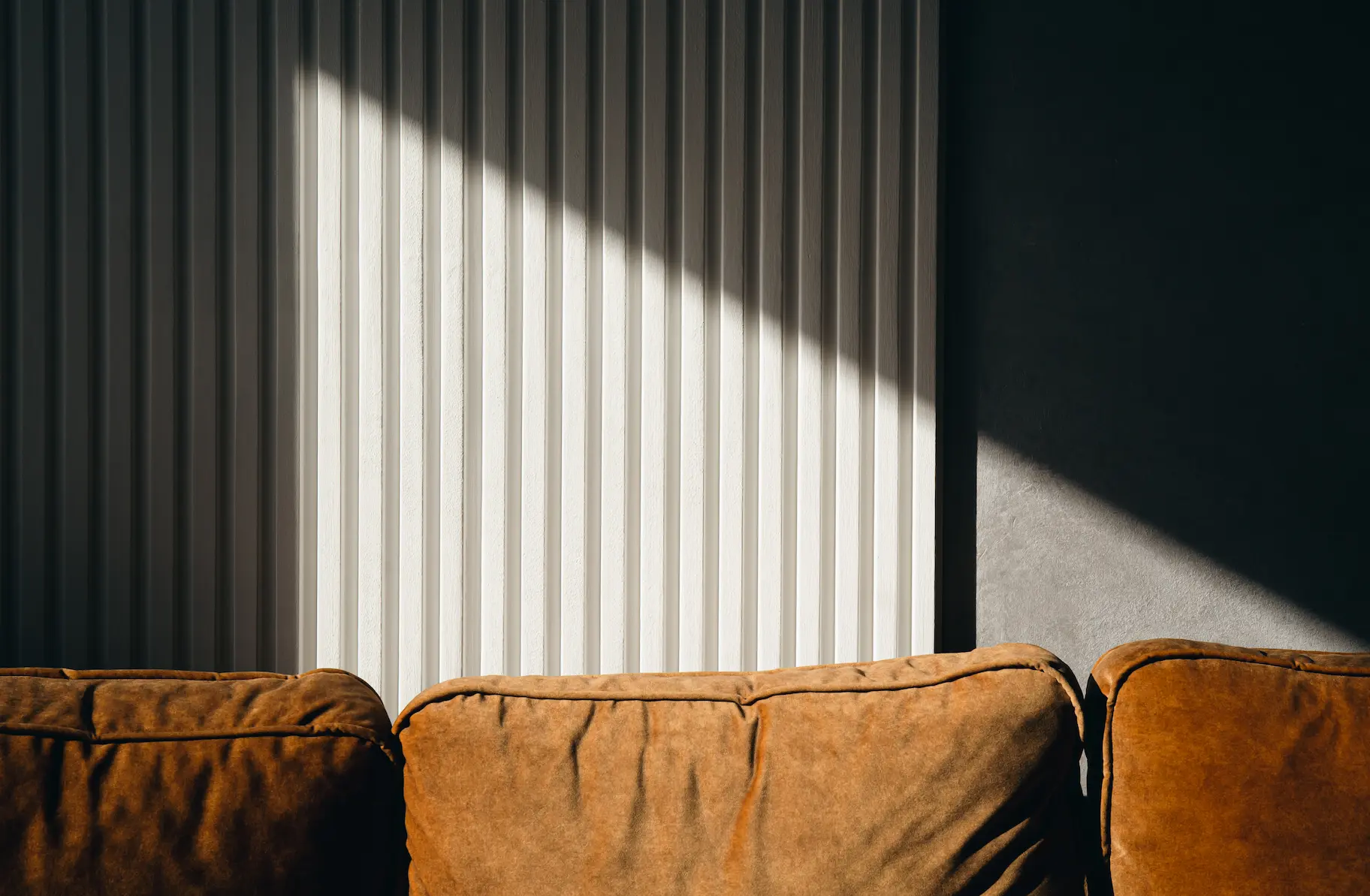 Rust-coloured velvet sofa against a white corrugated wall with diagonal sunlight