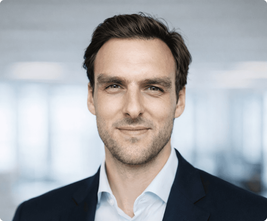 A man with glasses and a beard is looking directly at the camera, seated in a cozy, dimly lit café.