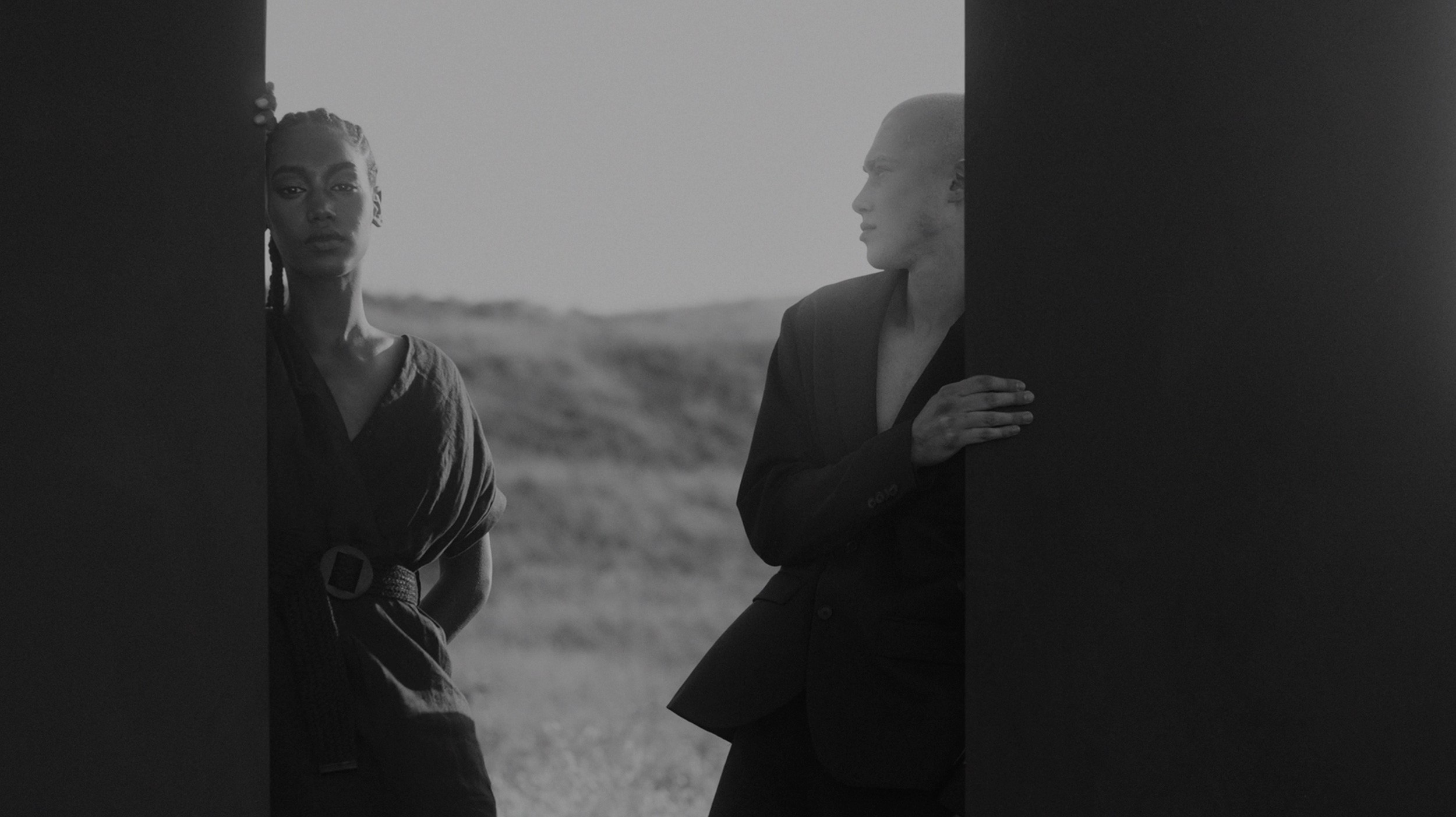 B/W photo: woman with braids (left) and man in suit (right) framed by dark panels.