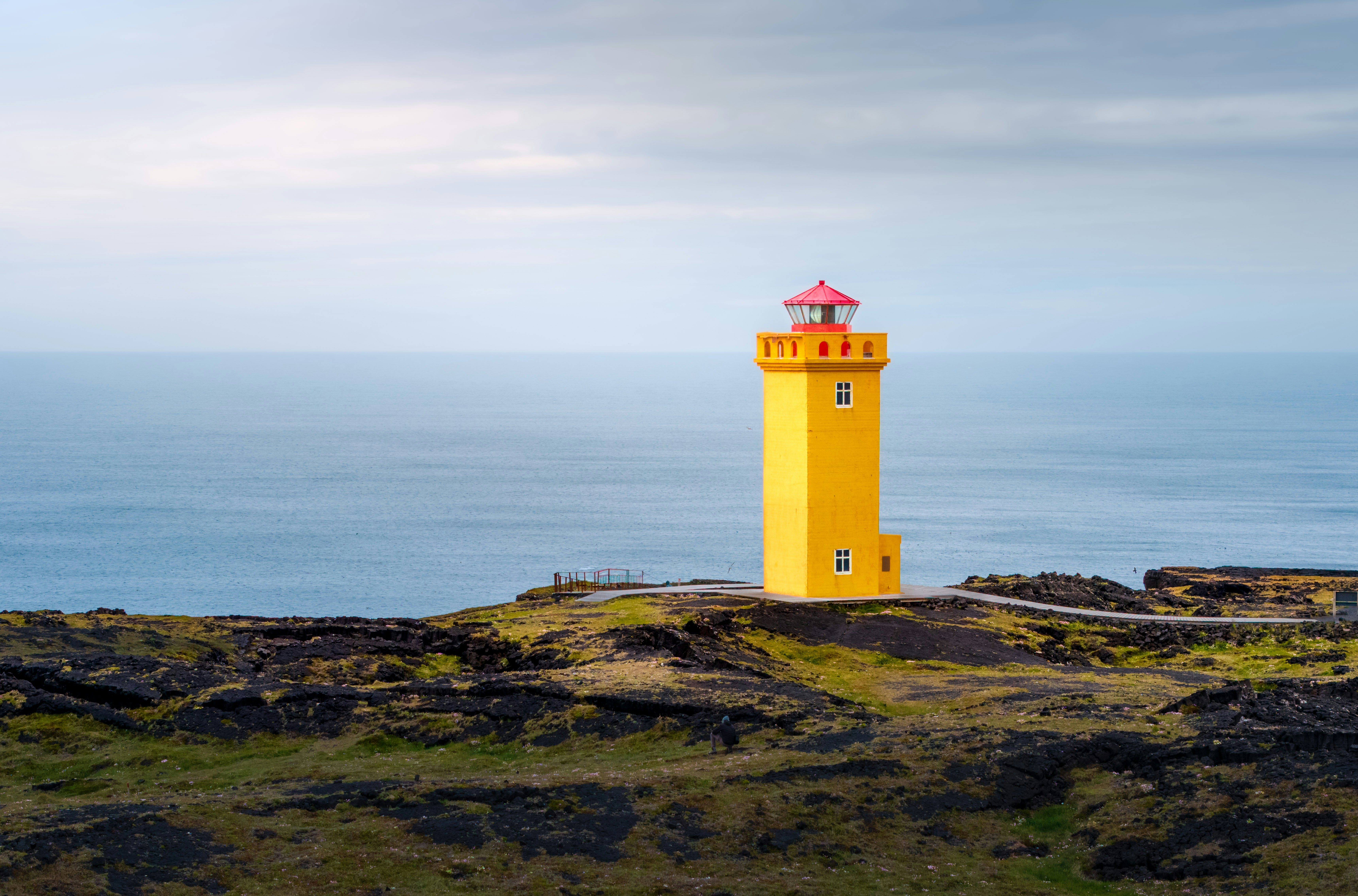 A bright yellow lighthouse stands overlooking the sea.