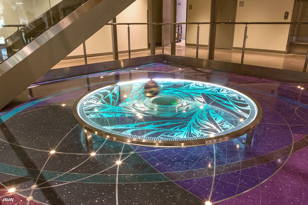 Foucault pendulum suspended above terrazzo floor with celestial patterns, illustrating time, gravity, and the rotation of the earth