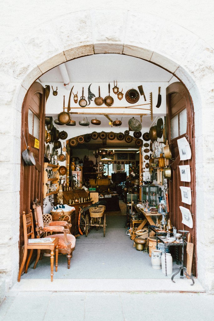 An antique shop brimming with vintage items and curiosities, including old cookware, furniture, and unique collectibles, inviting passersby to explore its nostalgic treasures.