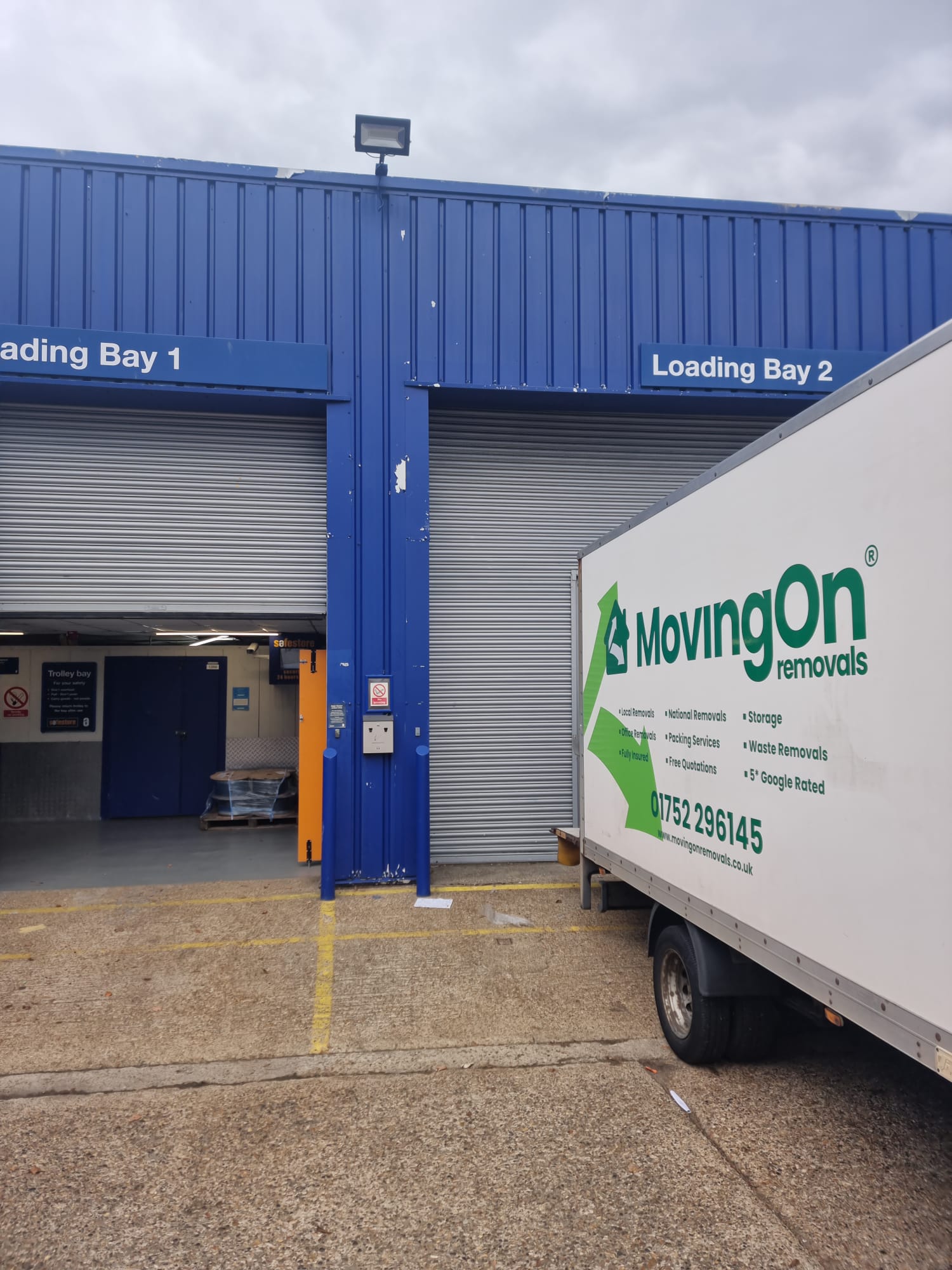 A MovingOn Removals truck backed up to a blue commercial storage facility loading bay, ready to unload items into secure self-storage.