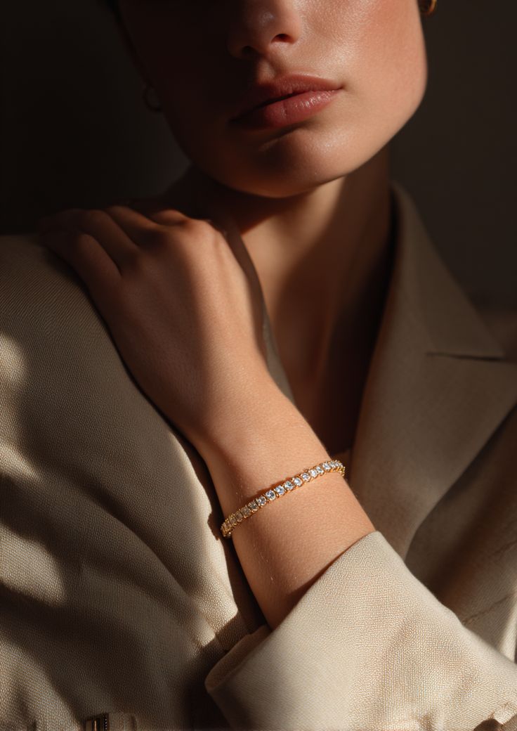 A woman wearing a beige blazer exudes elegance with a gold bracelet adorned with sparkling gemstones on her wrist, captured in soft, natural lighting.