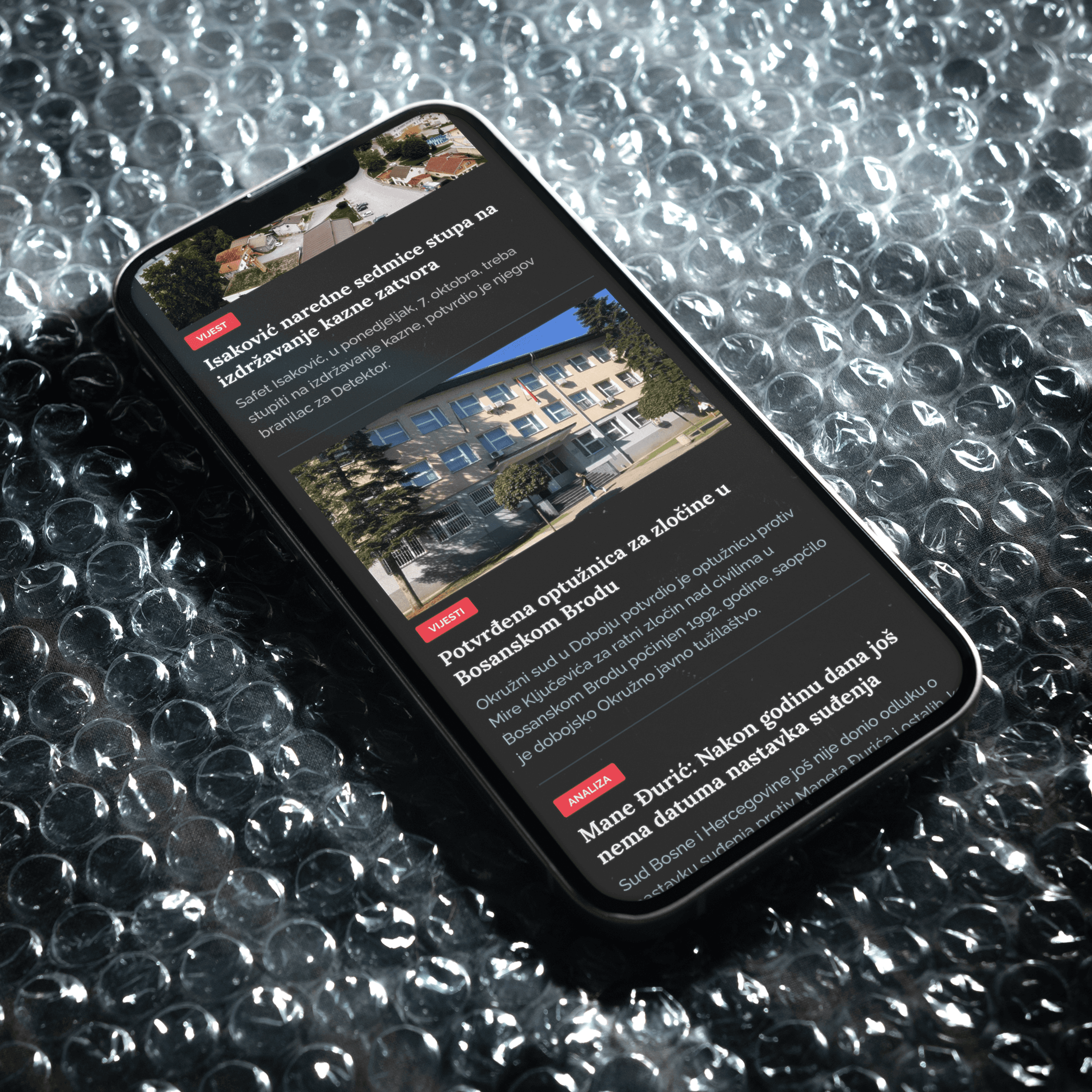 An iPhone placed on the sheet of bubble wrap, its display showing the mobile view of detektor.ba website.