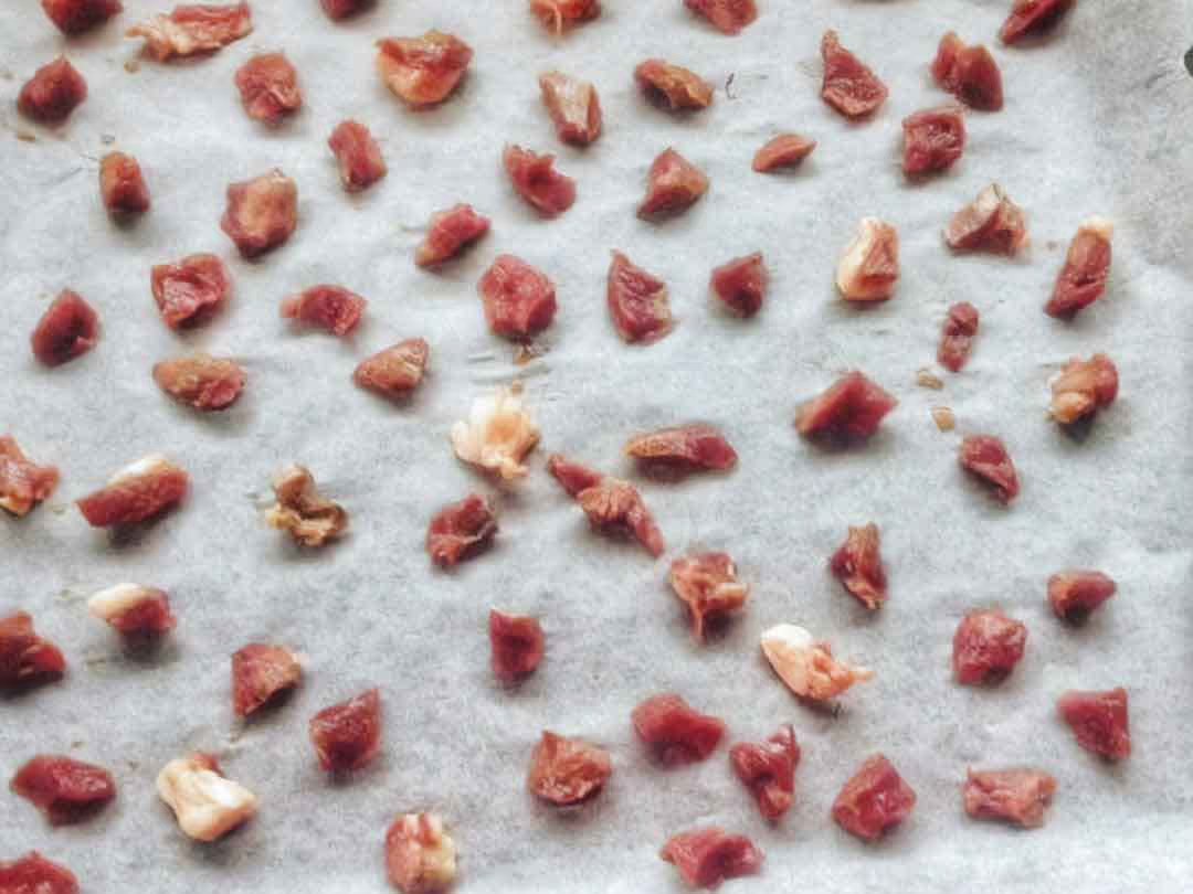 Diced pieces of meat spread evenly on parchment paper, ready for drying or baking.
