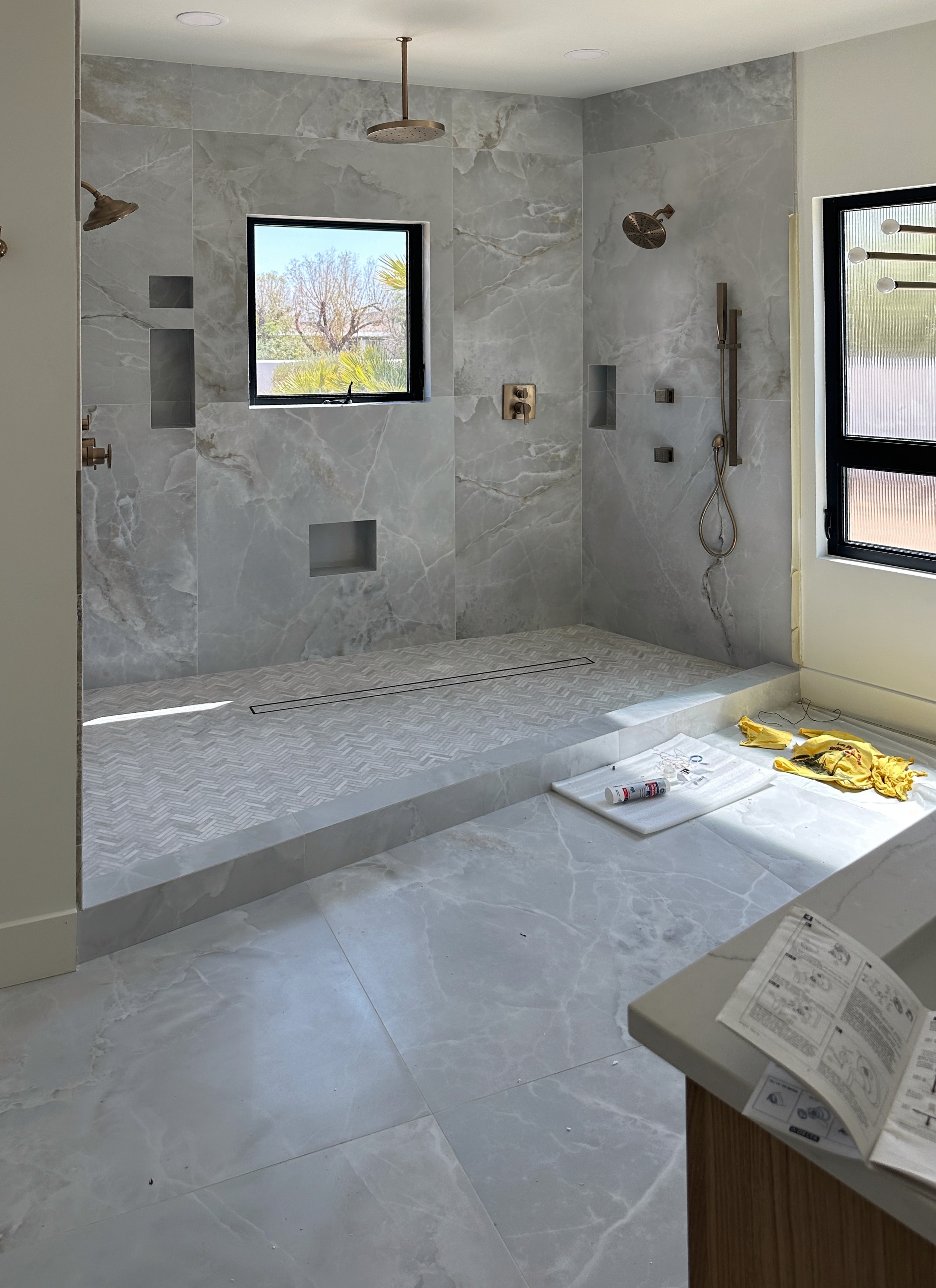 Contemporary bathroom shower with large format grey marble-look wall tiles, a textured linear drain shower floor, and matching grey large format floor tiles outside the shower, showcasing a sleek custom tile installation.