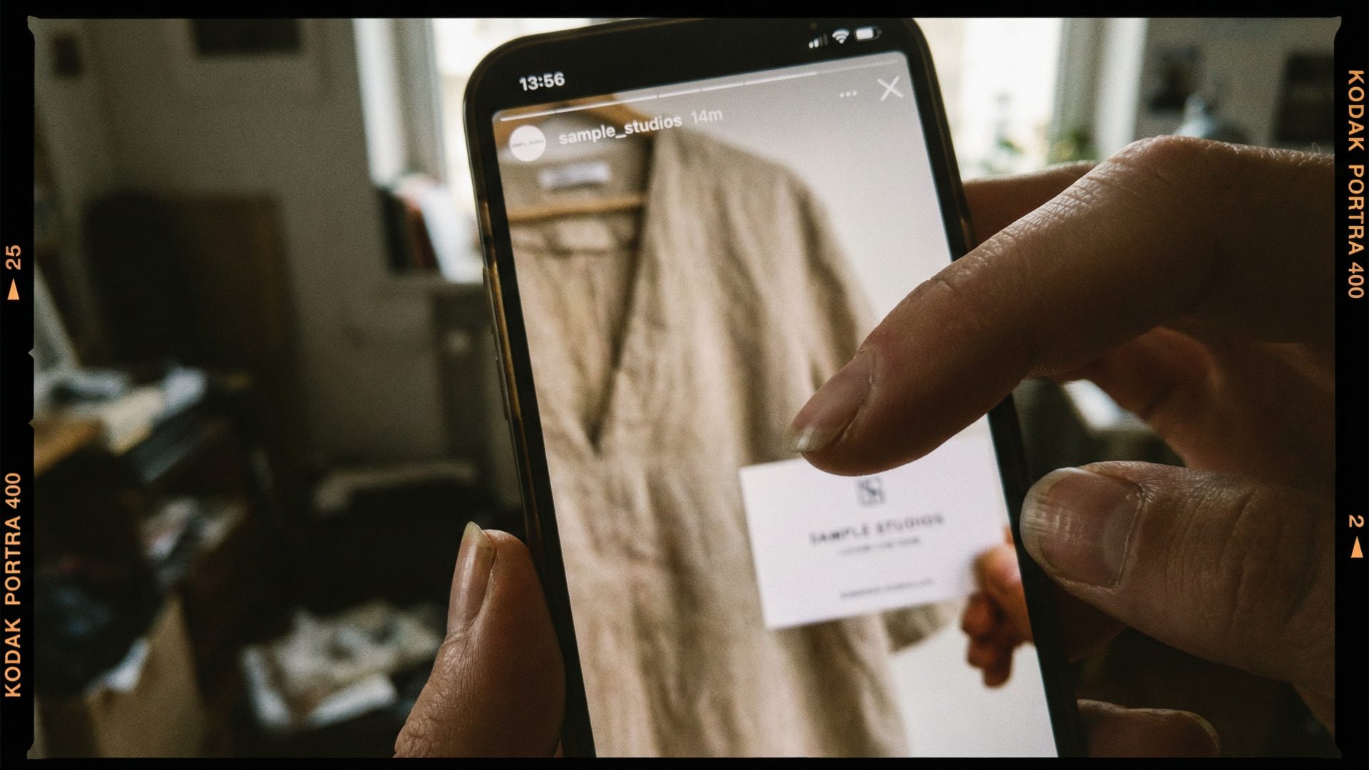 A close-up of a phone showing a blurry Instagram story from a clothing brand, where a sample card with supplier info is accidentally visible in the background. A finger zooms in to read the text.