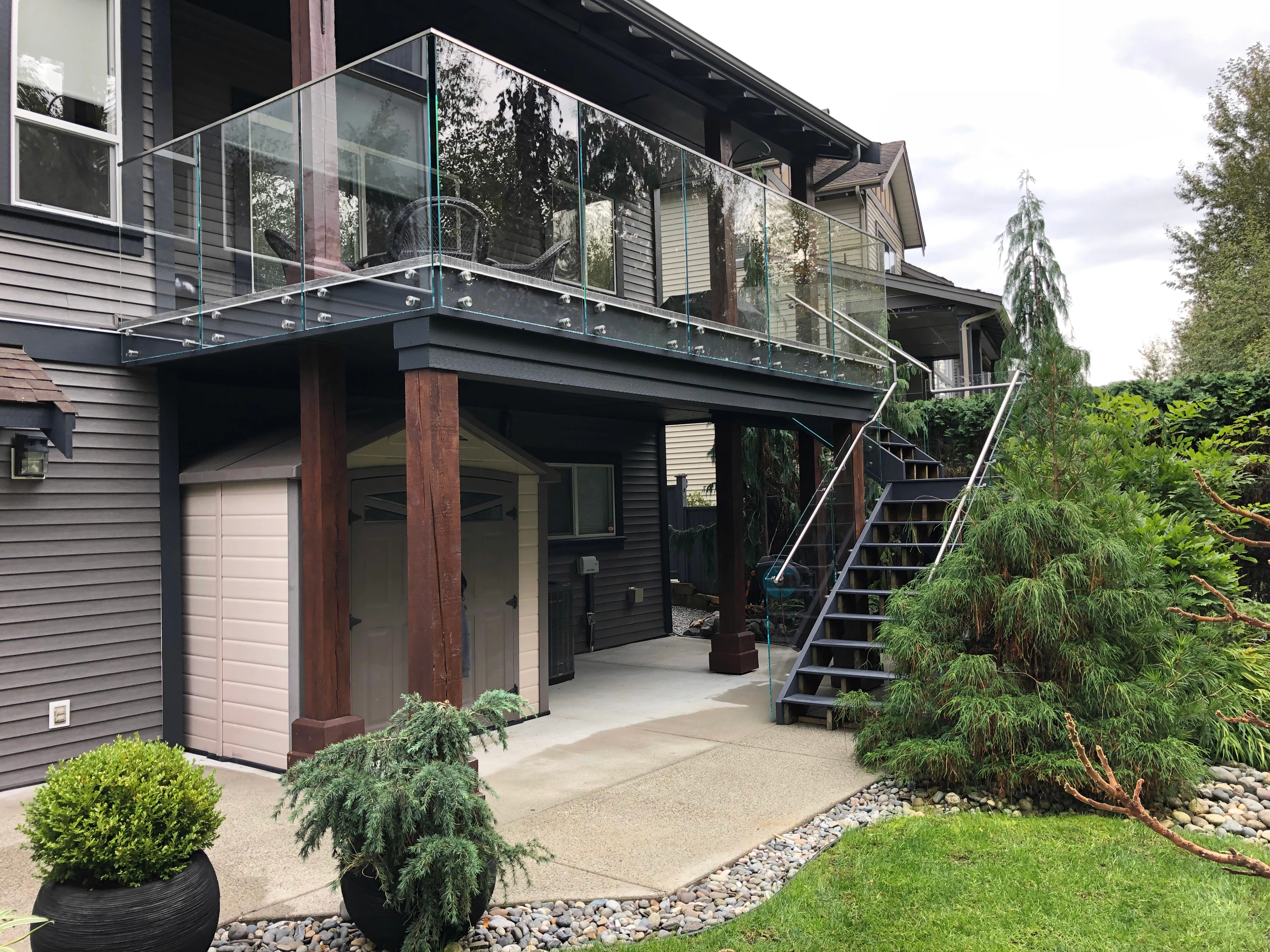Modern elevated deck with frameless glass railings mounted on exposed stainless steel standoff hardware.
