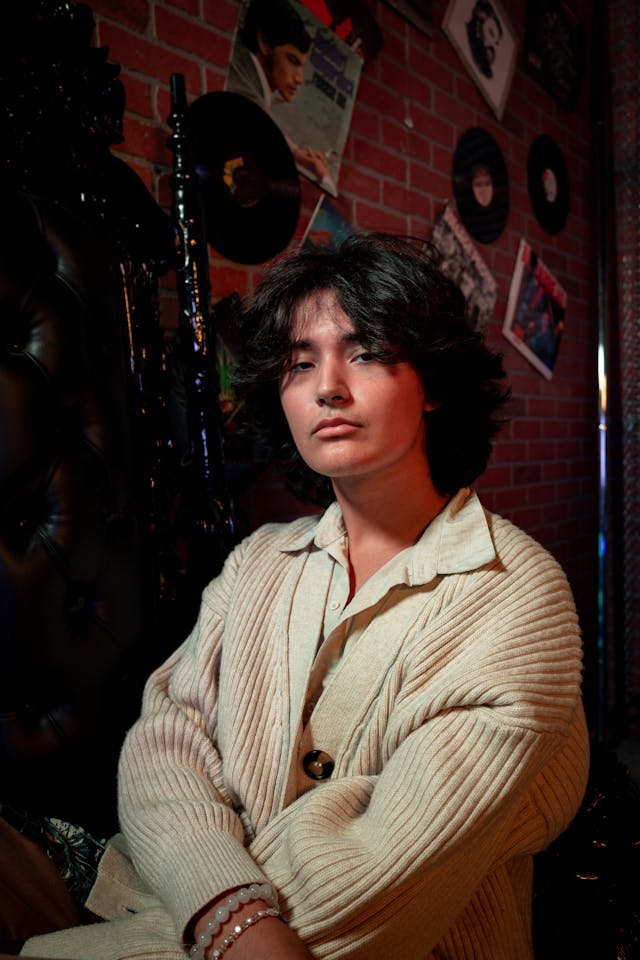 A person in a cream-colored cardigan sits in a dimly lit room