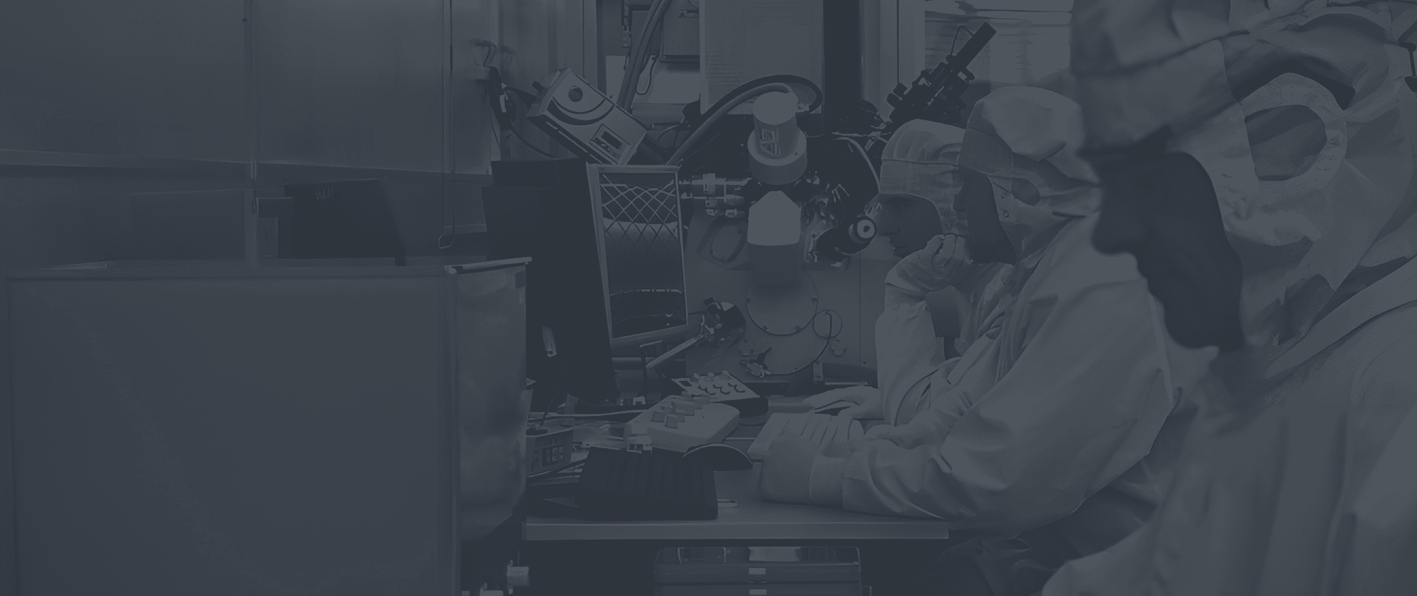 Engineers in cleanroom suits operating advanced microfabrication equipment in a laboratory setting.