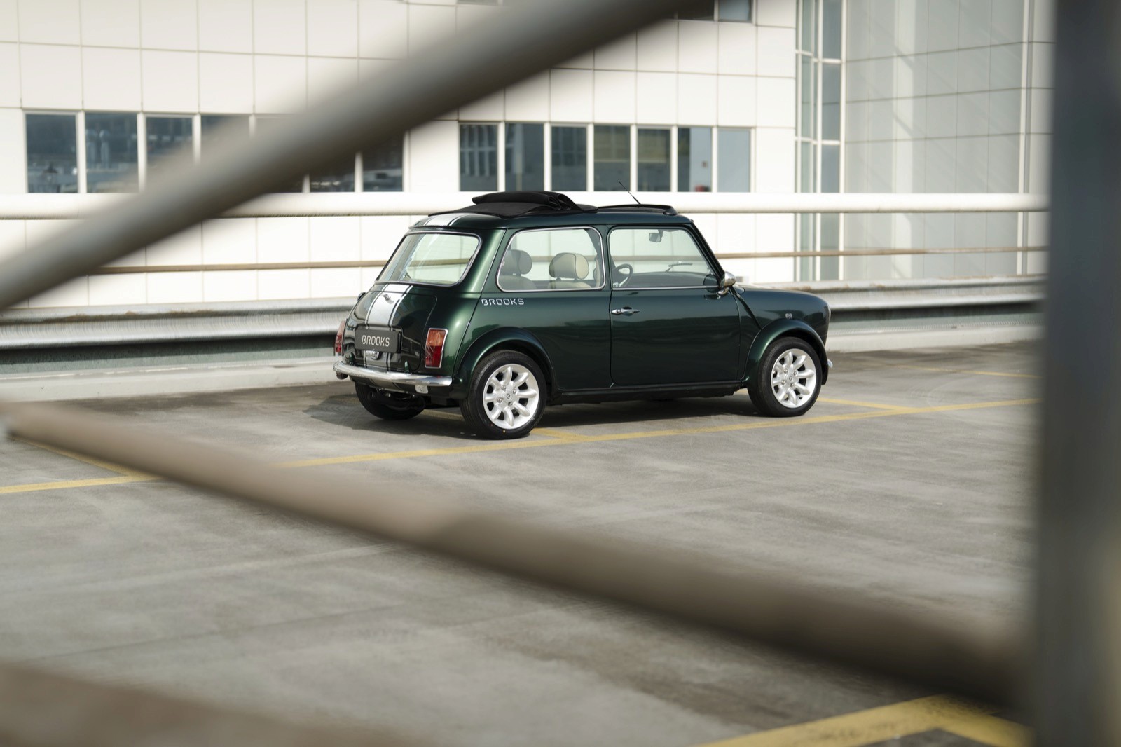 A small vintage car parked on a concrete surface, partially obscured by railing in the foreground.