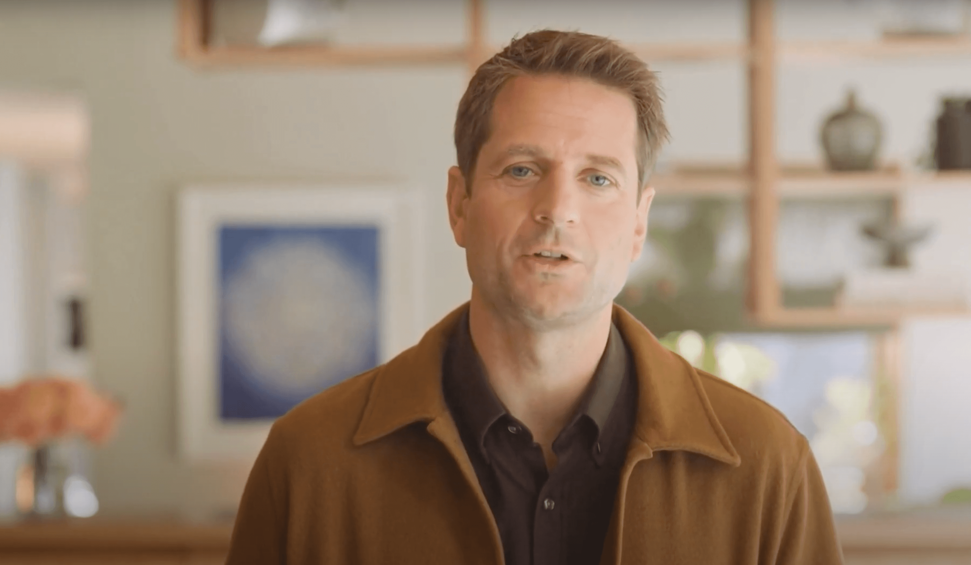 Klarna-CEO Sebastian Siemiatkowski in brauner Jacke spricht in einem Raum mit Regalen und abstrakter Kunst. Weiches Licht, neutrale Töne.