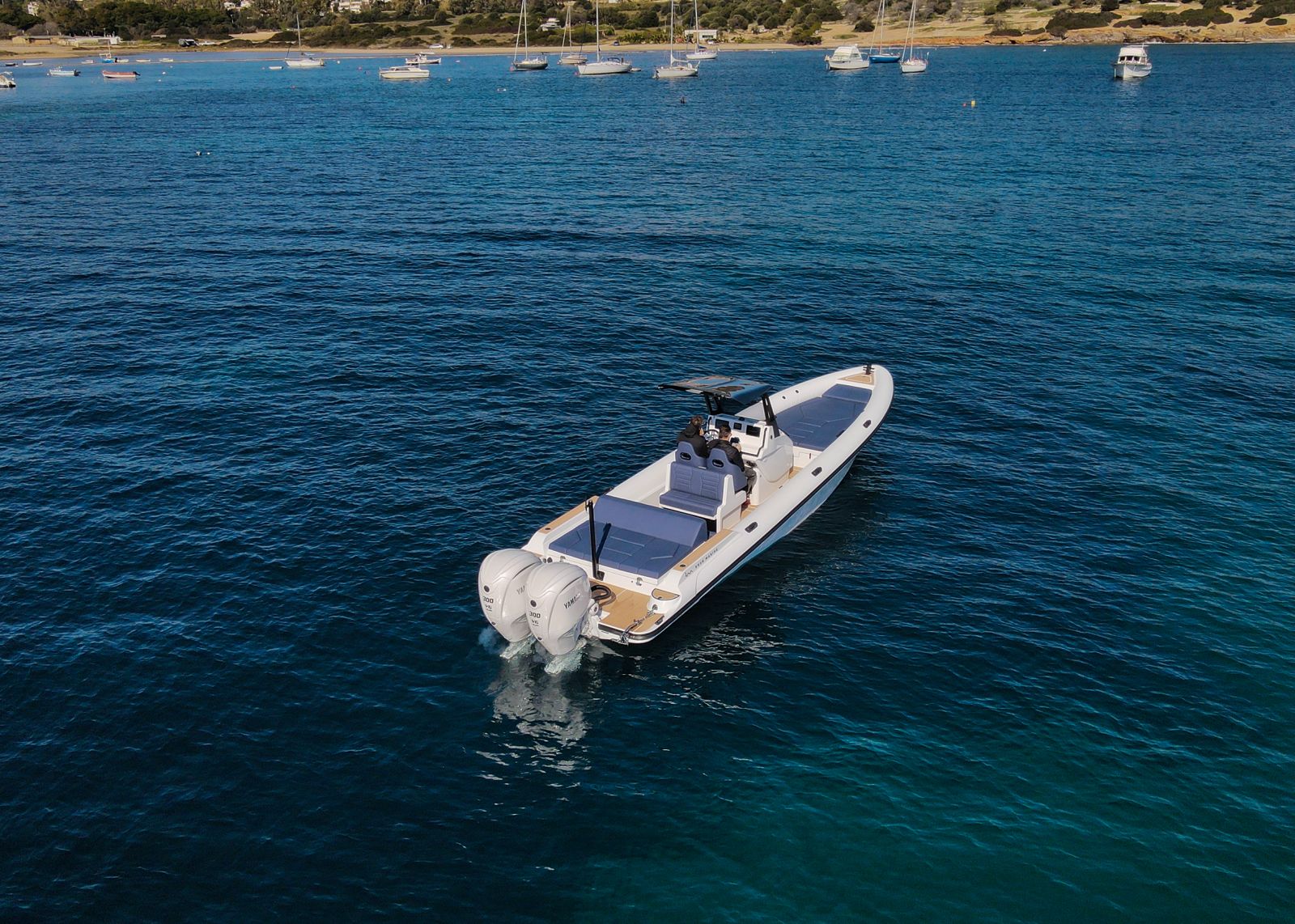 White Rock 36 speedboat with captain at helm cruising calm blue waters near Paros coastline with hills in background.