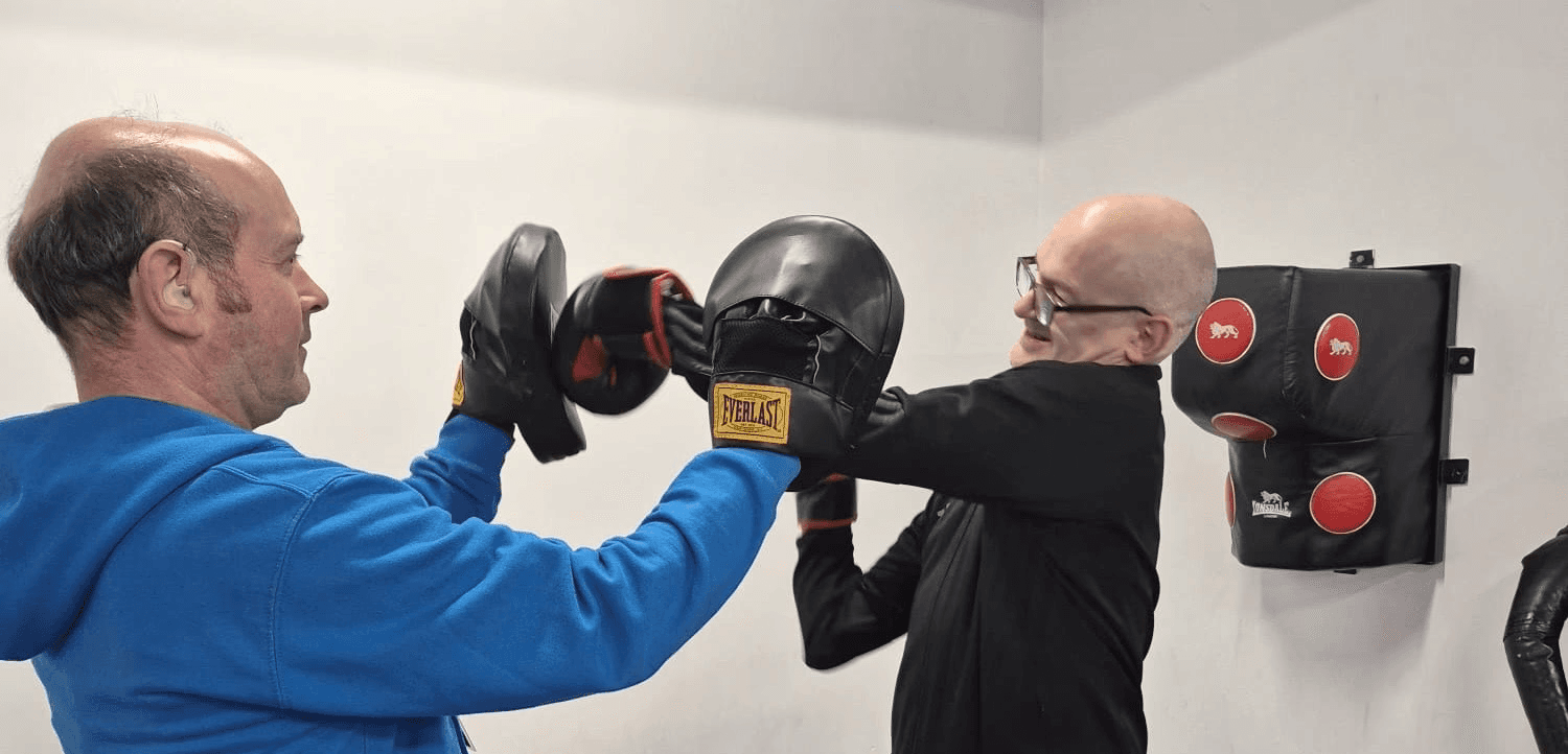 A support worker holding up boxing gloves and deaf client boxing