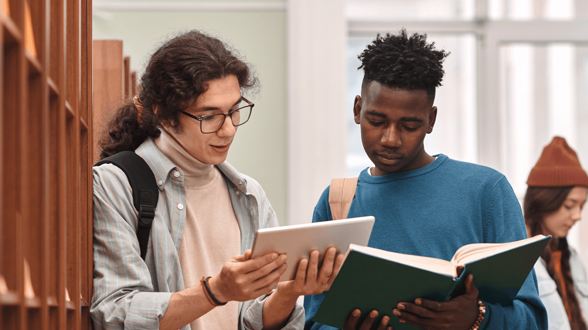 Two young people focused on educational activities: one reading a book and the other browsing on a tablet