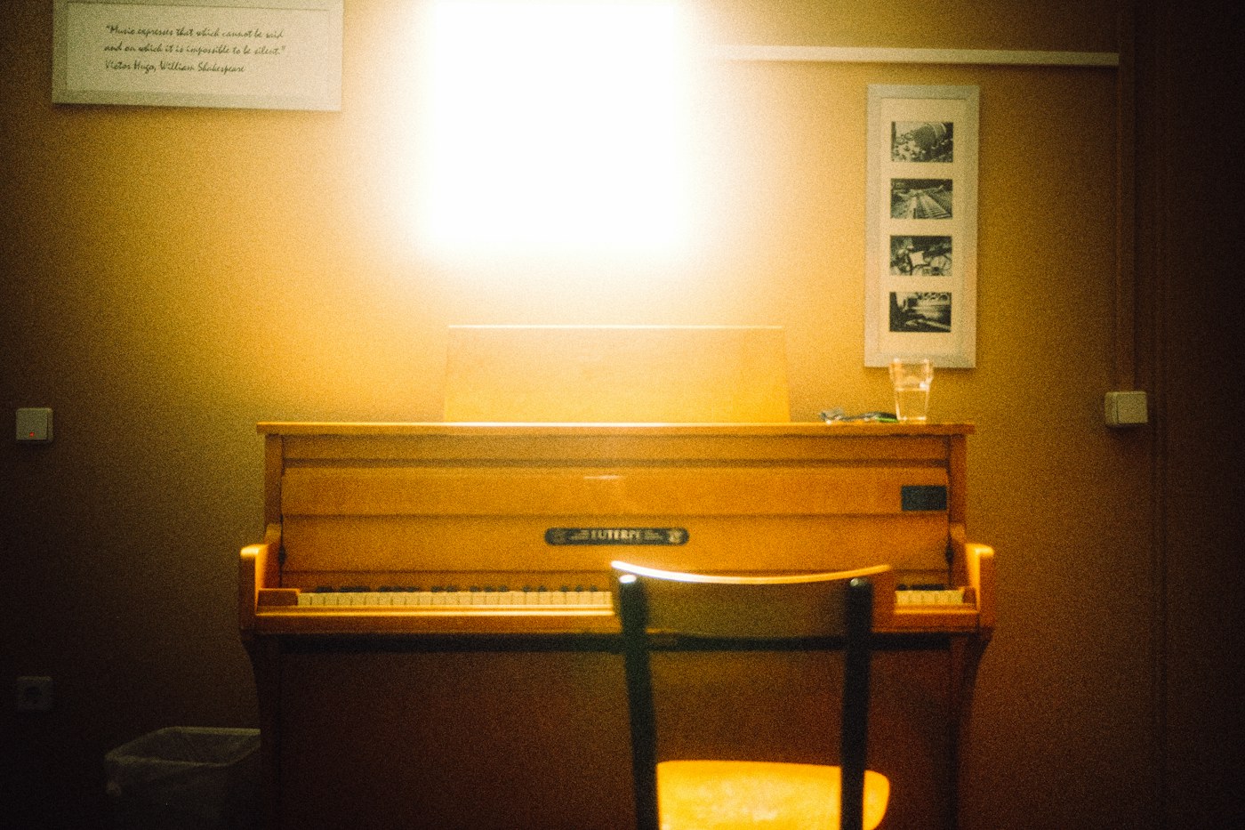 A wooden upright piano and a chair in a warm, sunlit lesson room