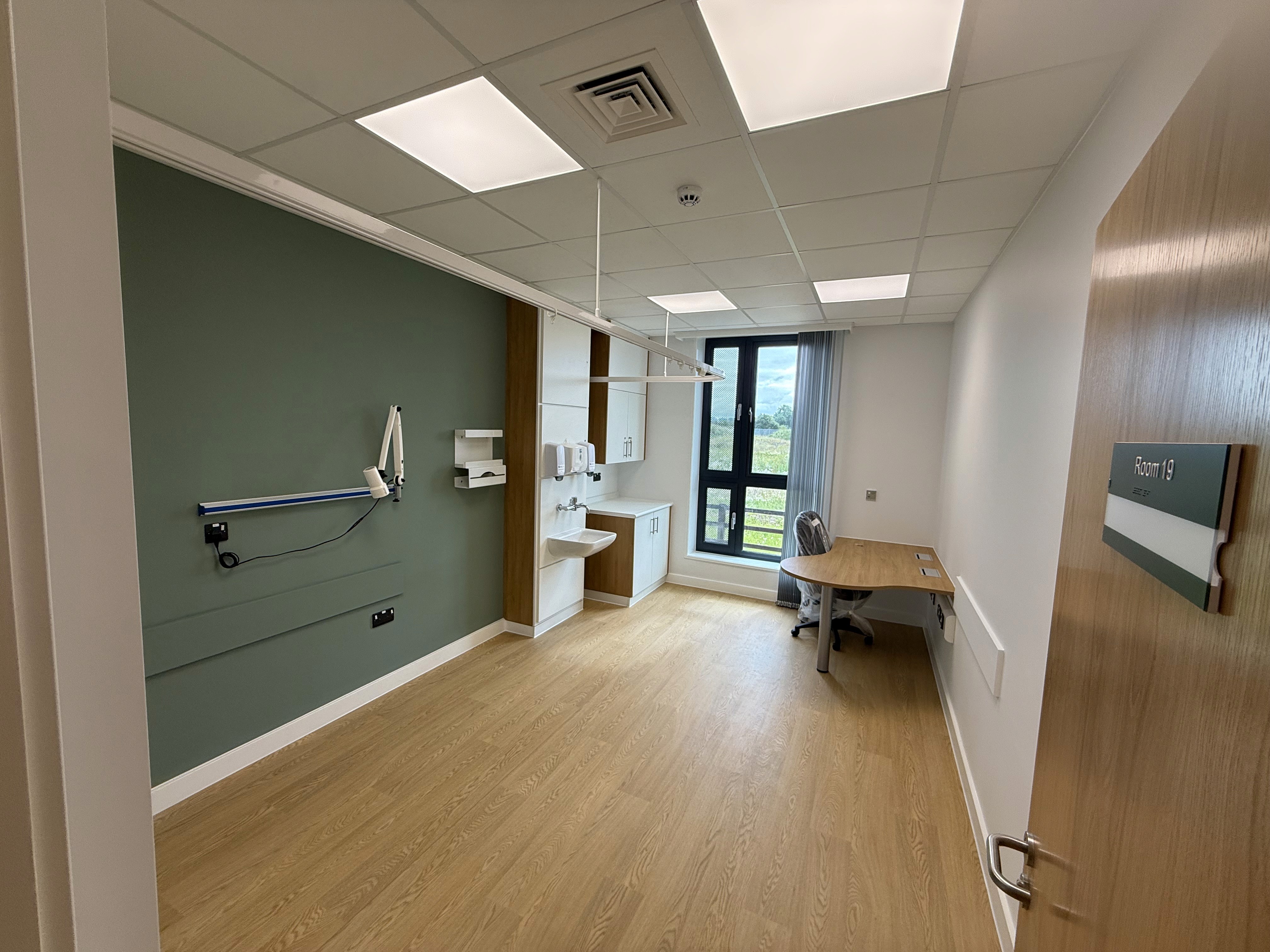 GP consulting room with sage green feature wall and wood-effect flooring at Marsh Court Health Centre, Leominster