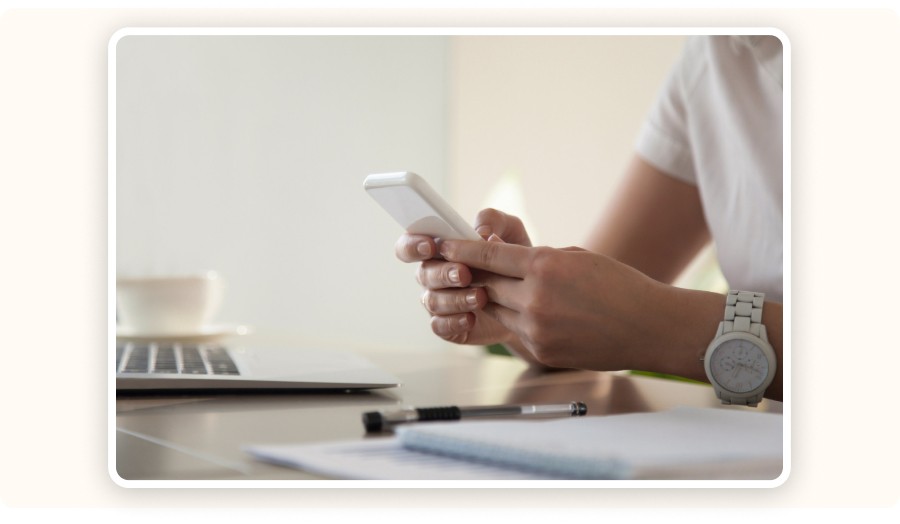 Person using smartphone at desk with laptop and notebook