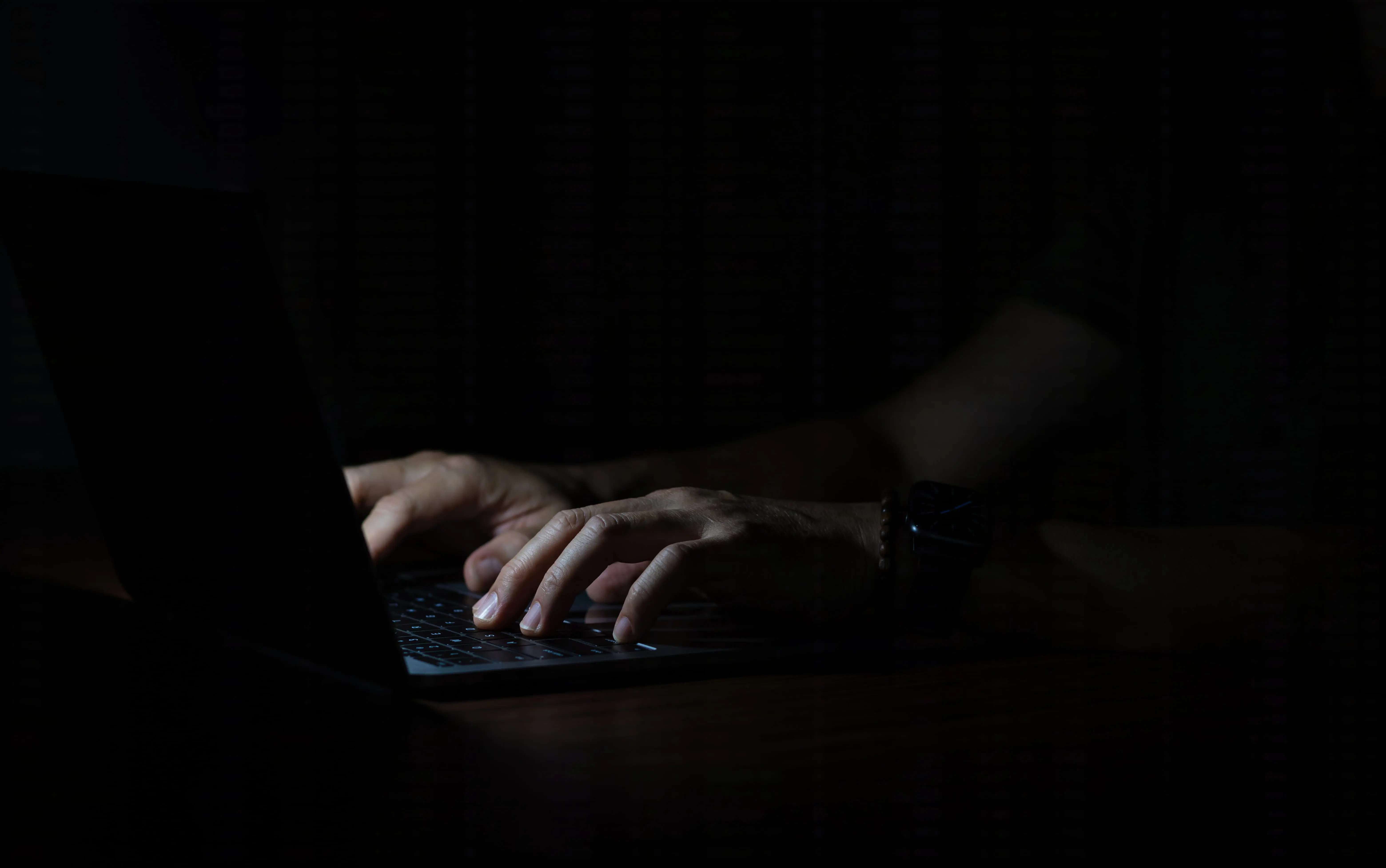 Close-up of hands typing on a laptop in a dark room.