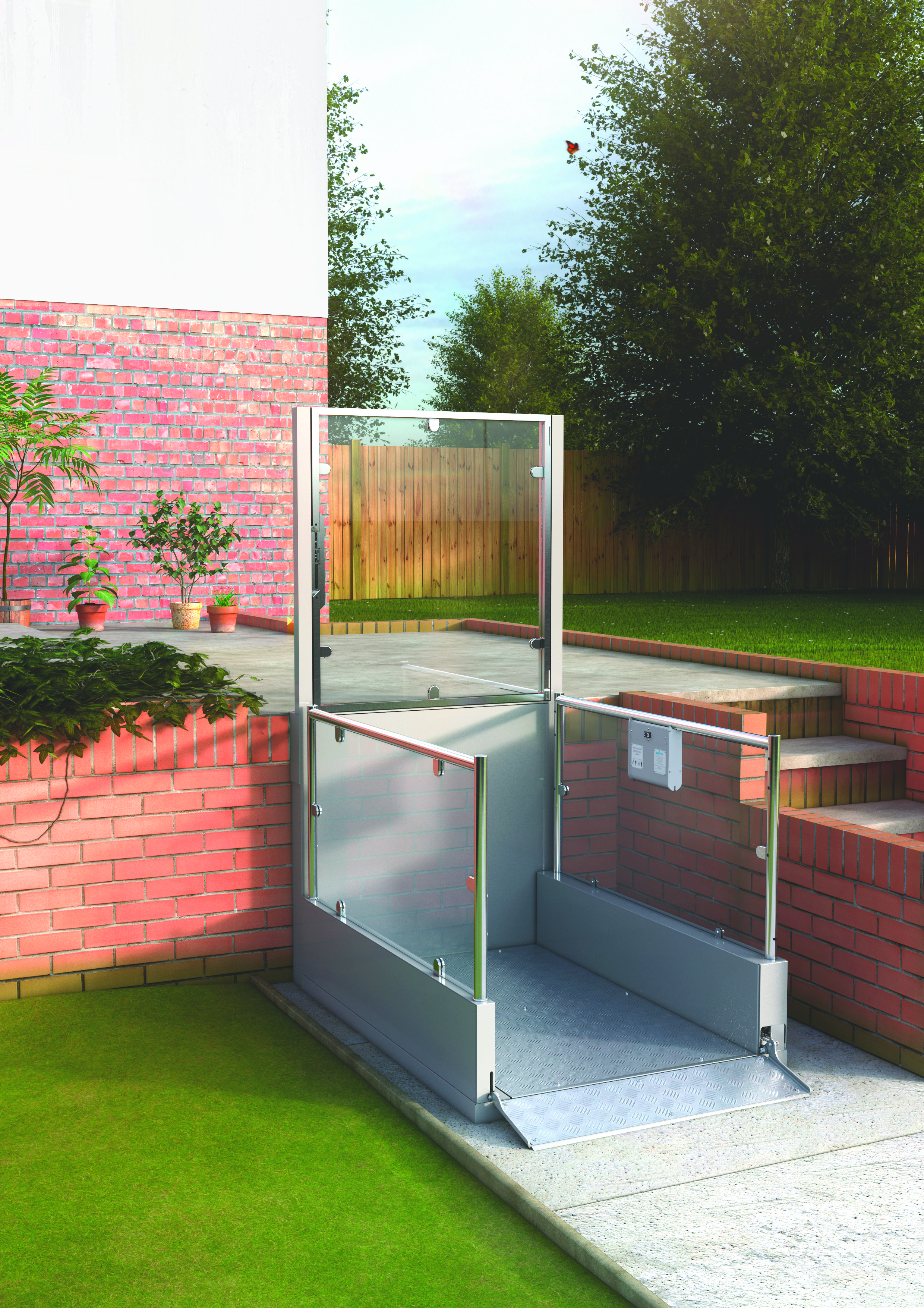 Outdoor vertical platform lift with full glass enclosure installed against a red brick garden wall — stainless steel frame with anti-slip chequer plate platform at lower garden level