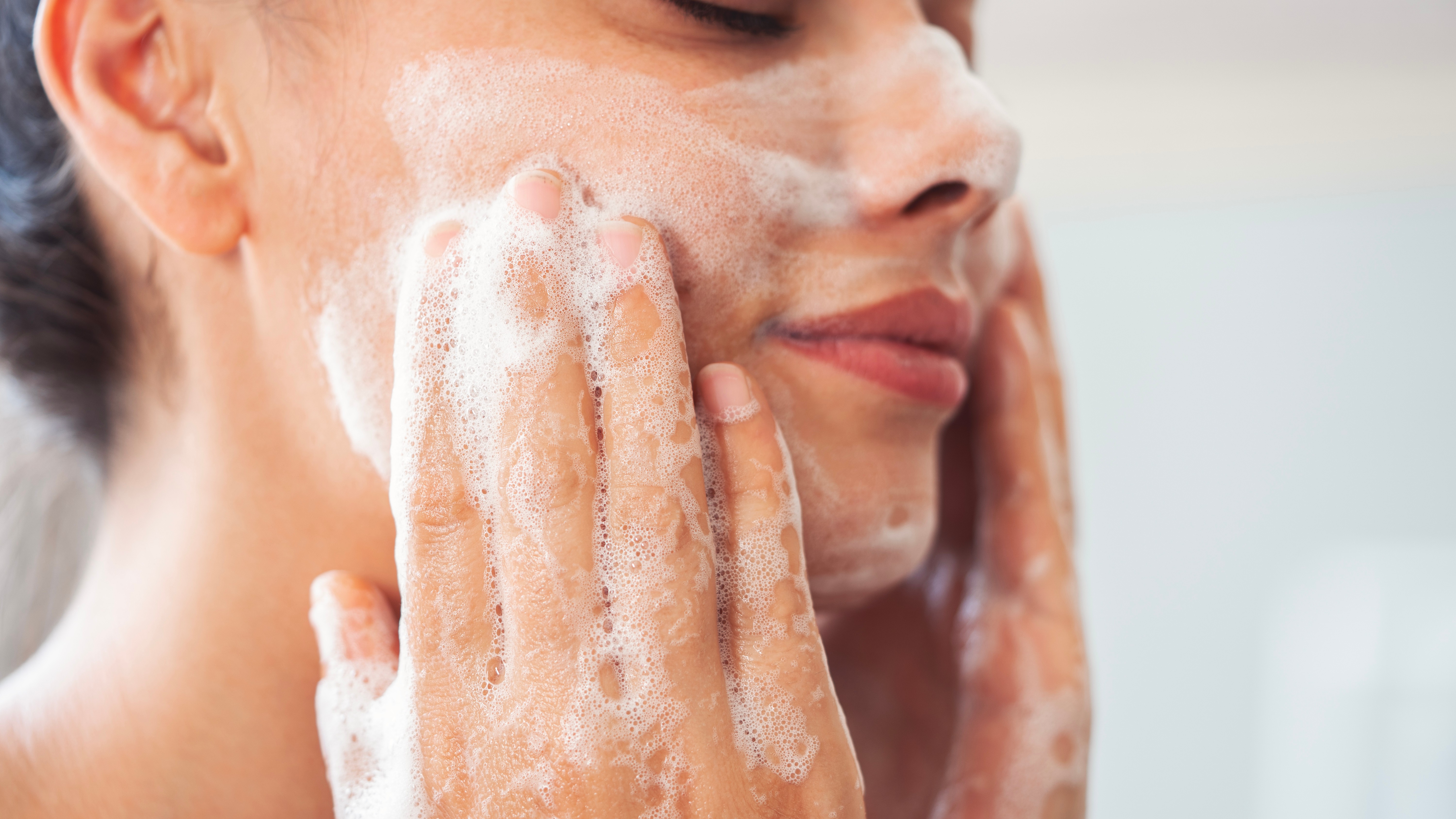 Woman washing face with cleanser and bubbles.