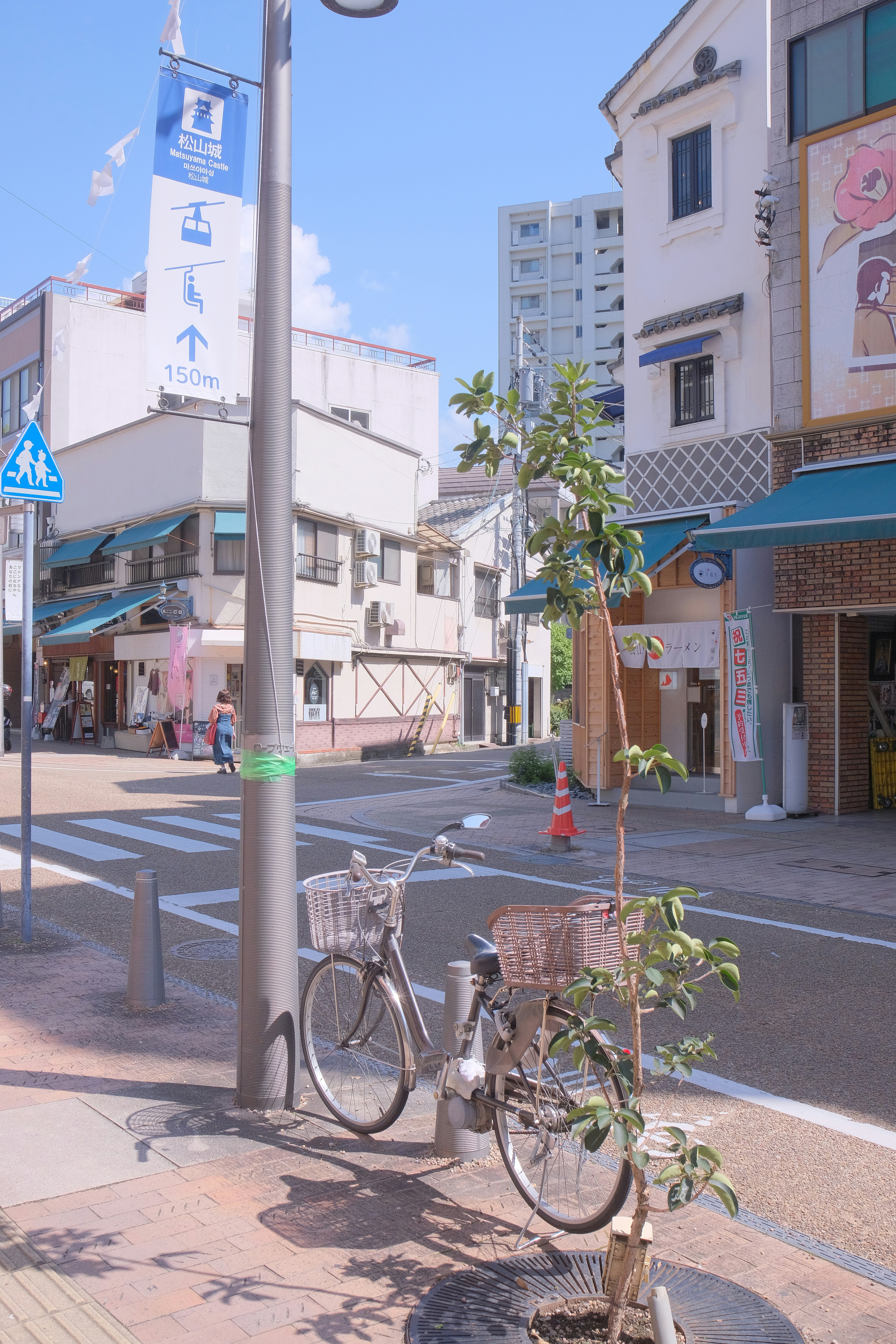 A street scene with buildings, a palm tree, and a clear blue sky, suggesting a warm and sunny day.