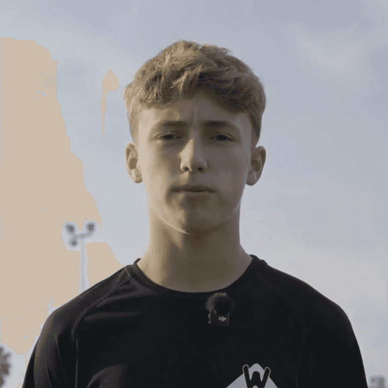 Person in black top posing with hand under chin in urban alleyway, blurred buildings behind