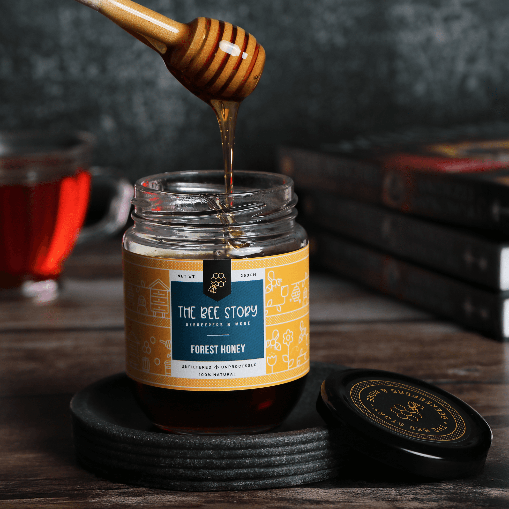 A jar of honey on a wooden table with a honey dipper drizzling honey, surrounded by books.