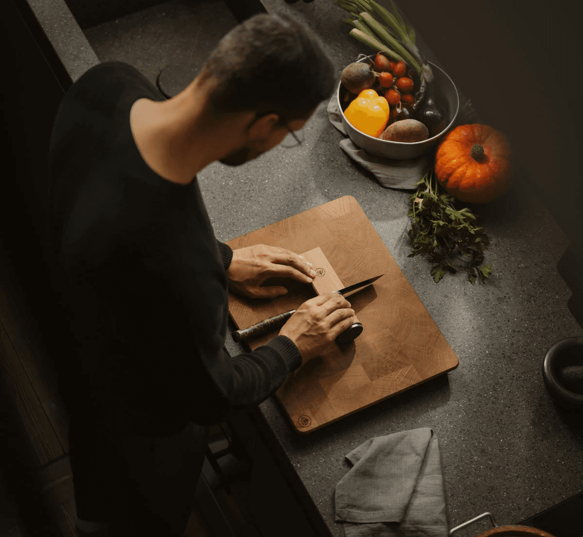 A man is sharpening a knife with the HORL3 Oak on the HORL Board on a kitchen counter.