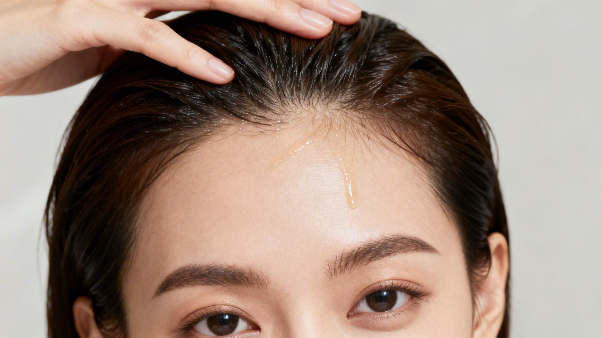 A close-up shows a hand applying a liquid hair treatment product to a person's wet scalp.