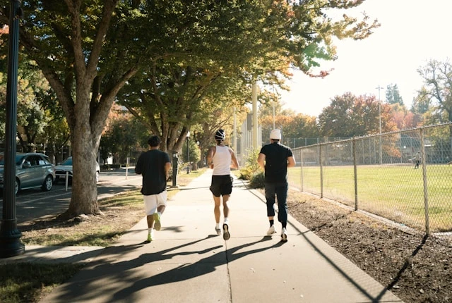Three people jogging down a tree-lined residential street