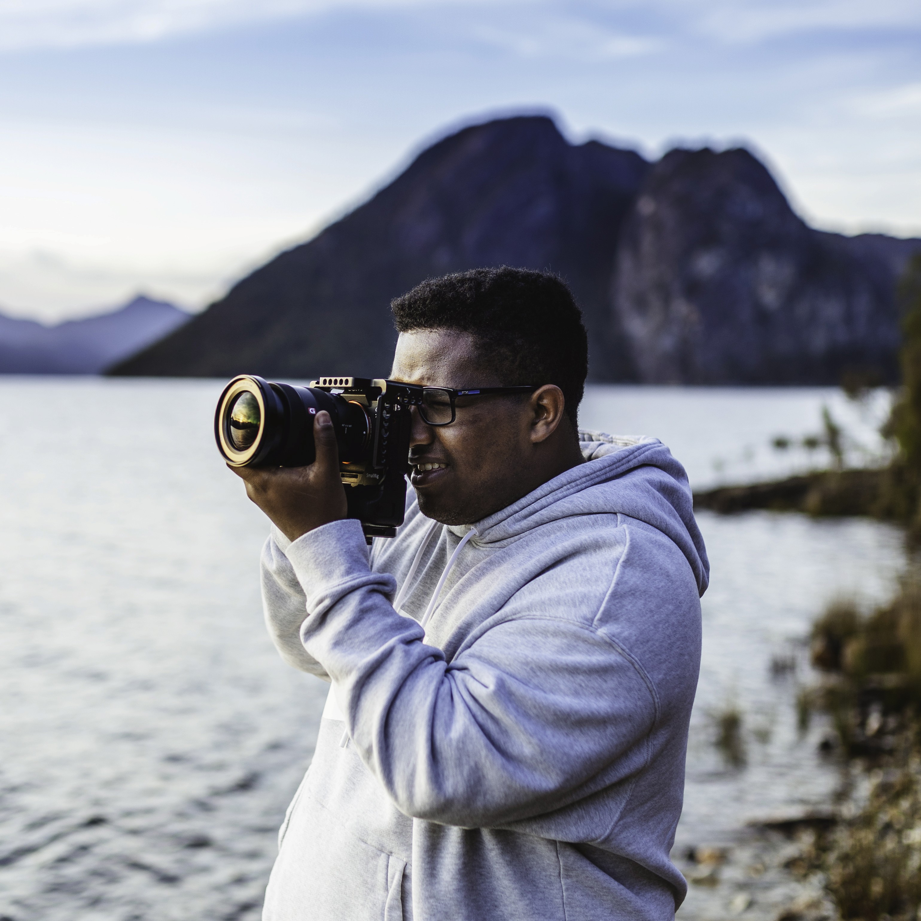 Two camera operators in a dimly lit studio adjust a large video camera. They wear headsets and caps, focusing intently. Mood is professional and focused.