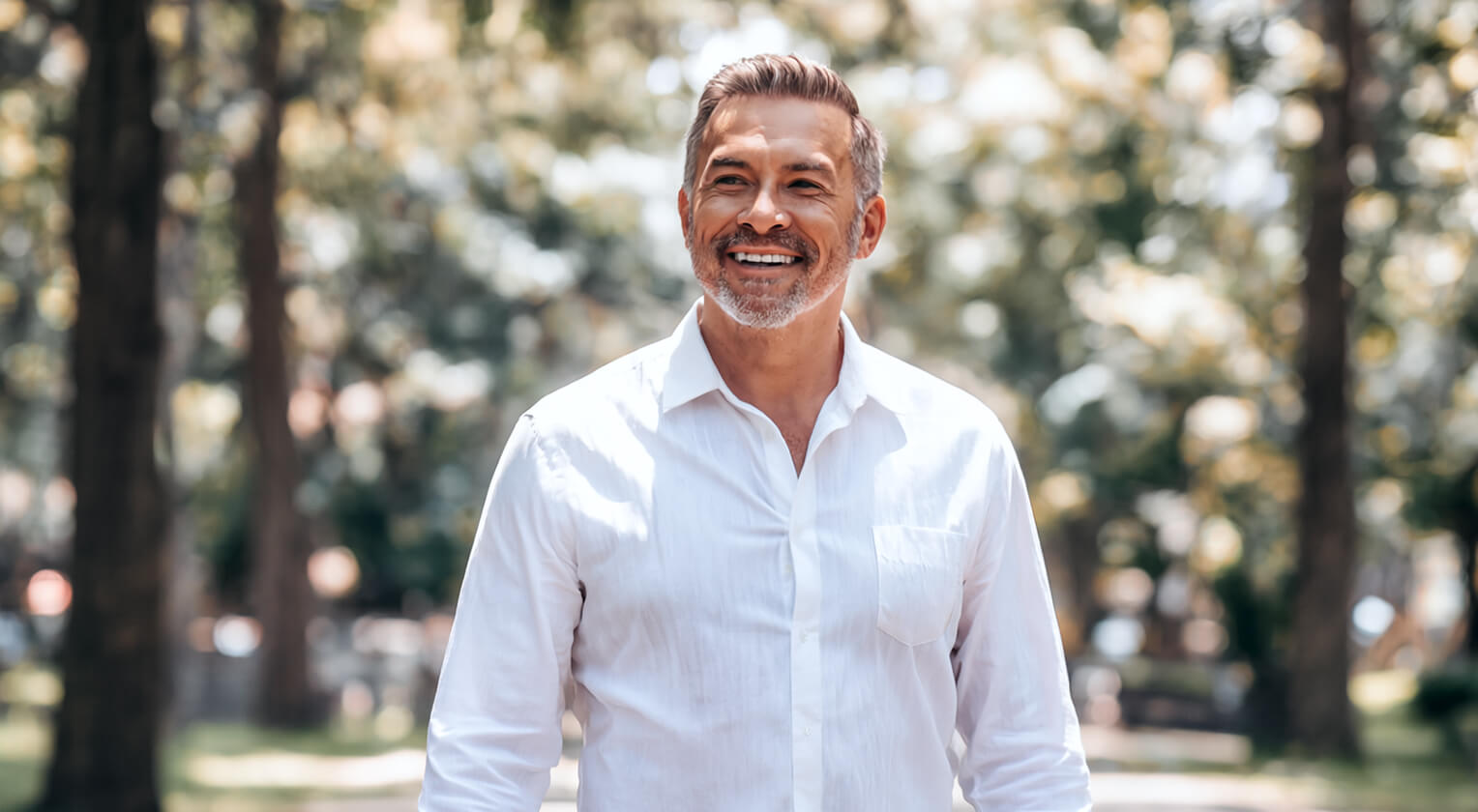 A middle aged man smiling with trees behind him