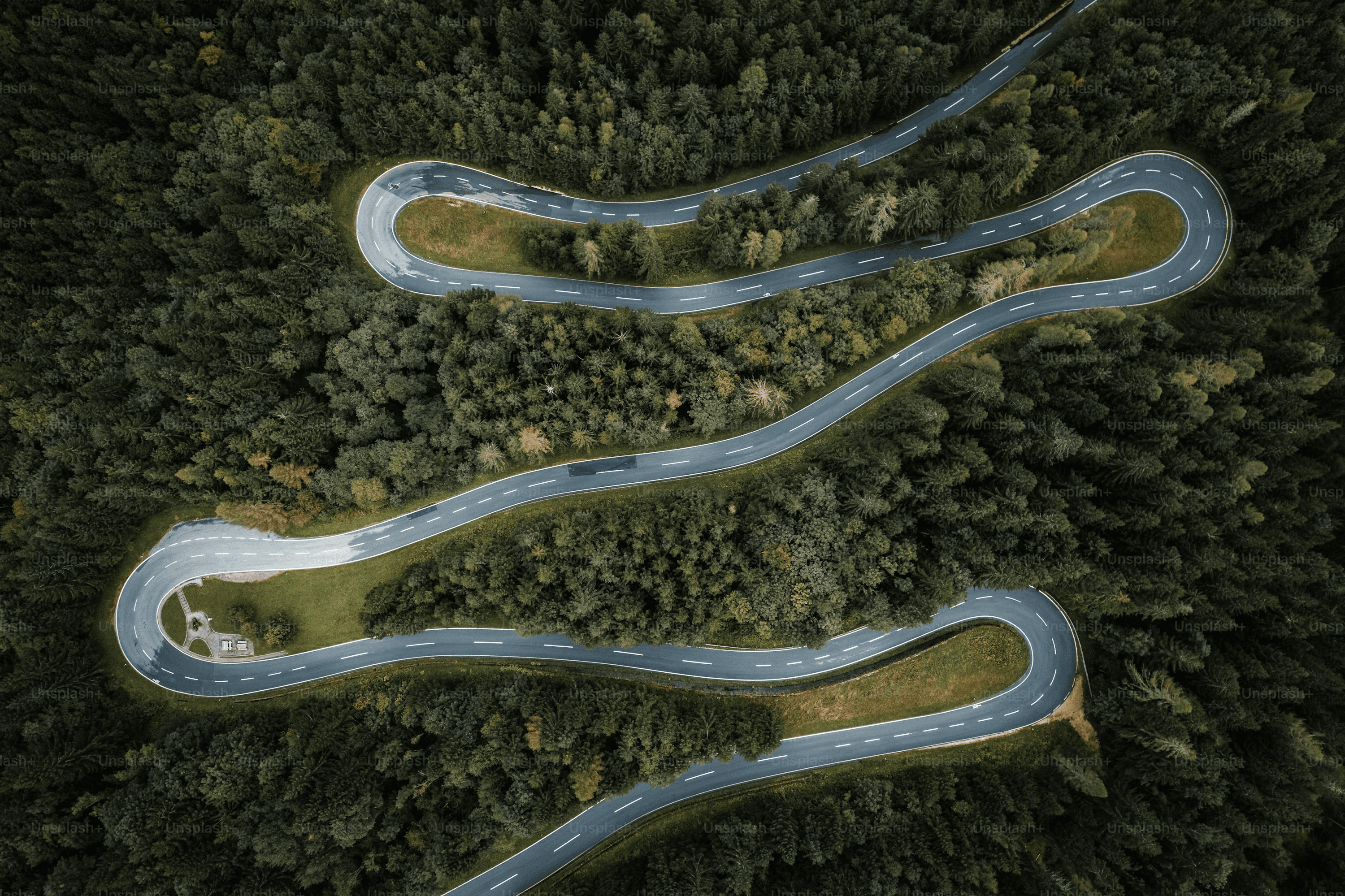 A winding road cuts through rocky terrain, surrounded by patches of green grass and illuminated by sunlight.