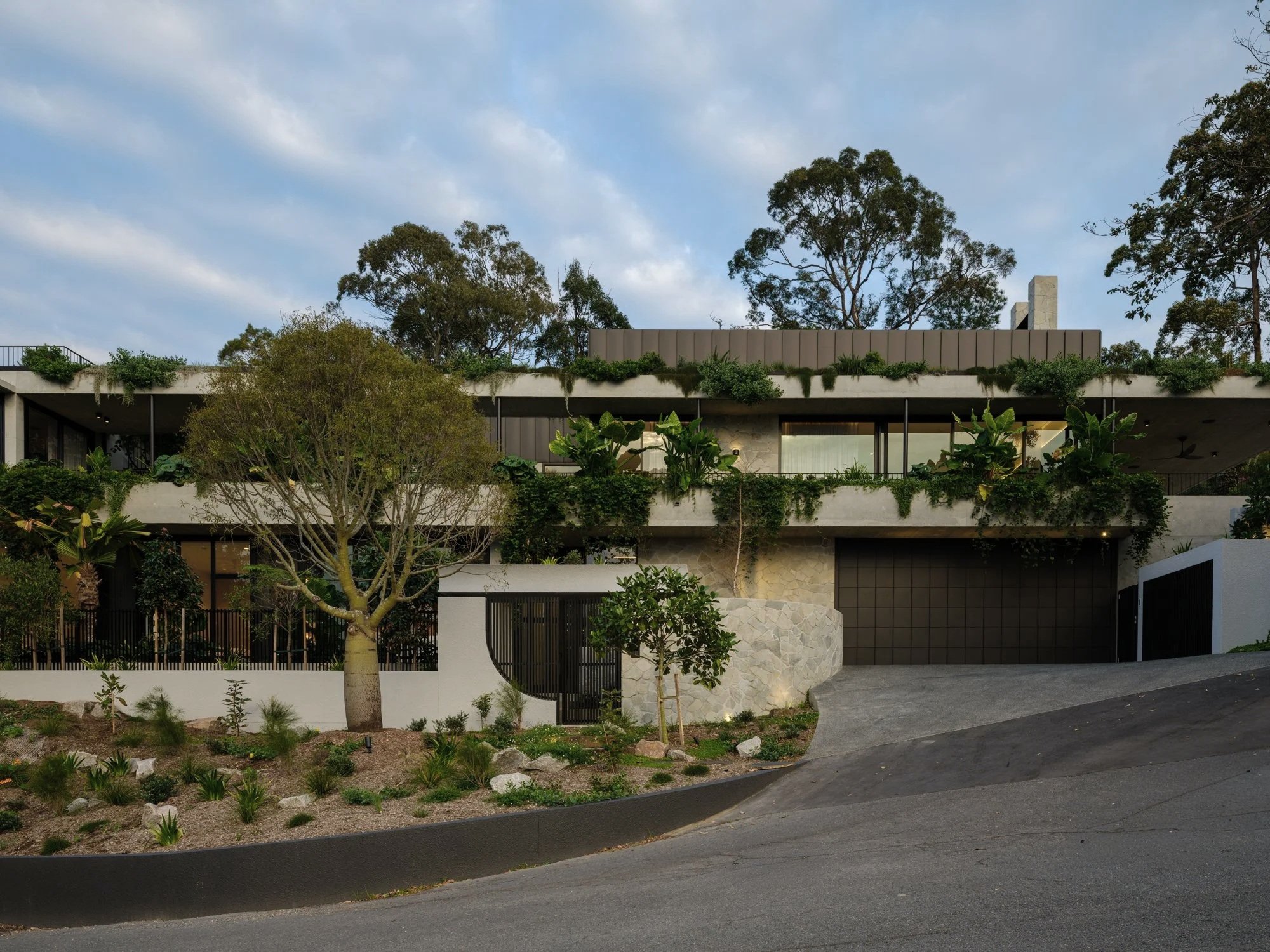 Modern multi-level residence with planted terraces, curved driveway, and integrated garage.