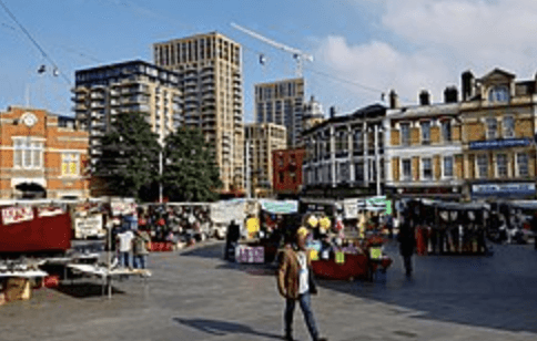 A smiling man with curly hair is sitting at a desk, looking at the camera, with a laptop and a lamp in the background.