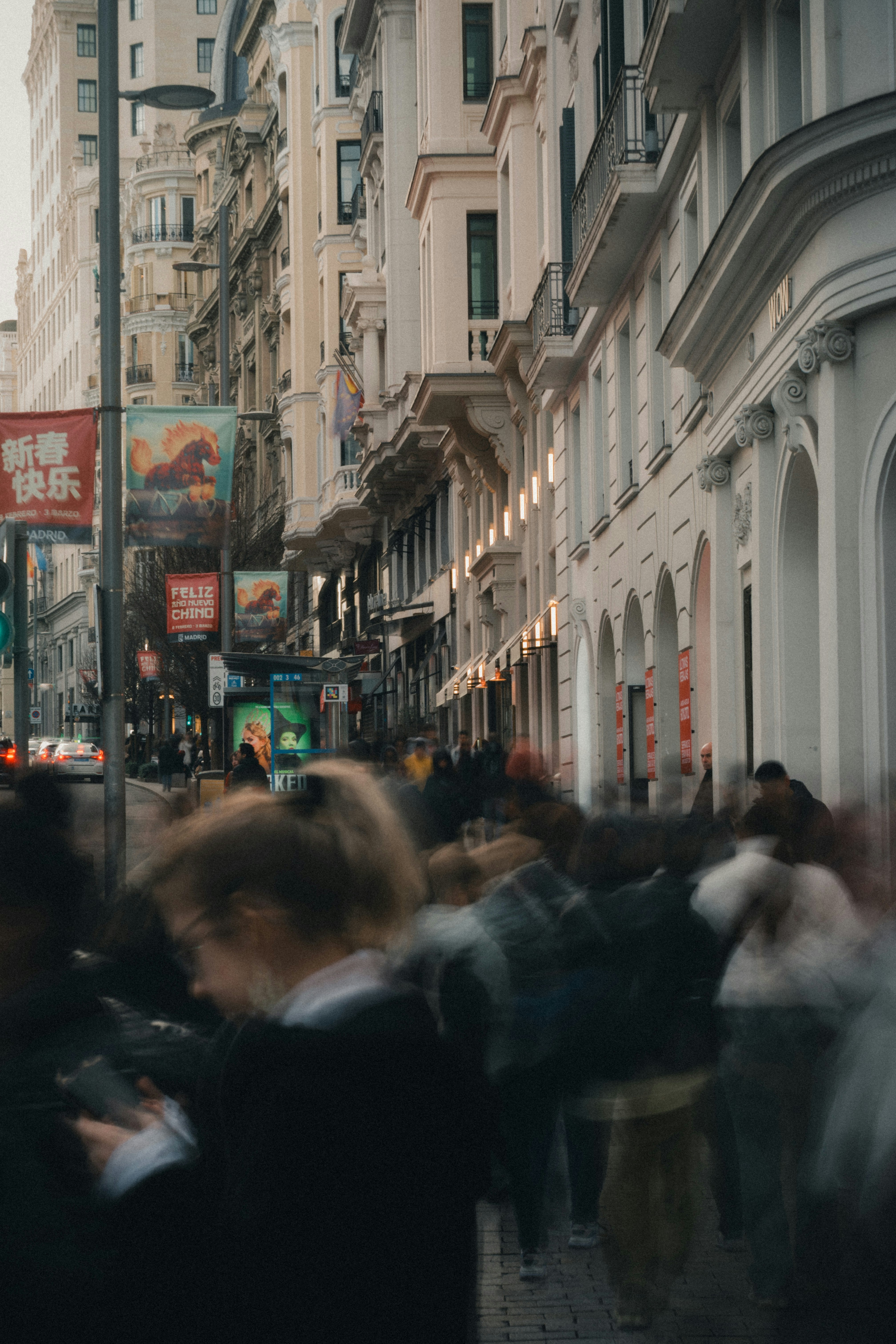 Blurred figures walk down a busy city street.