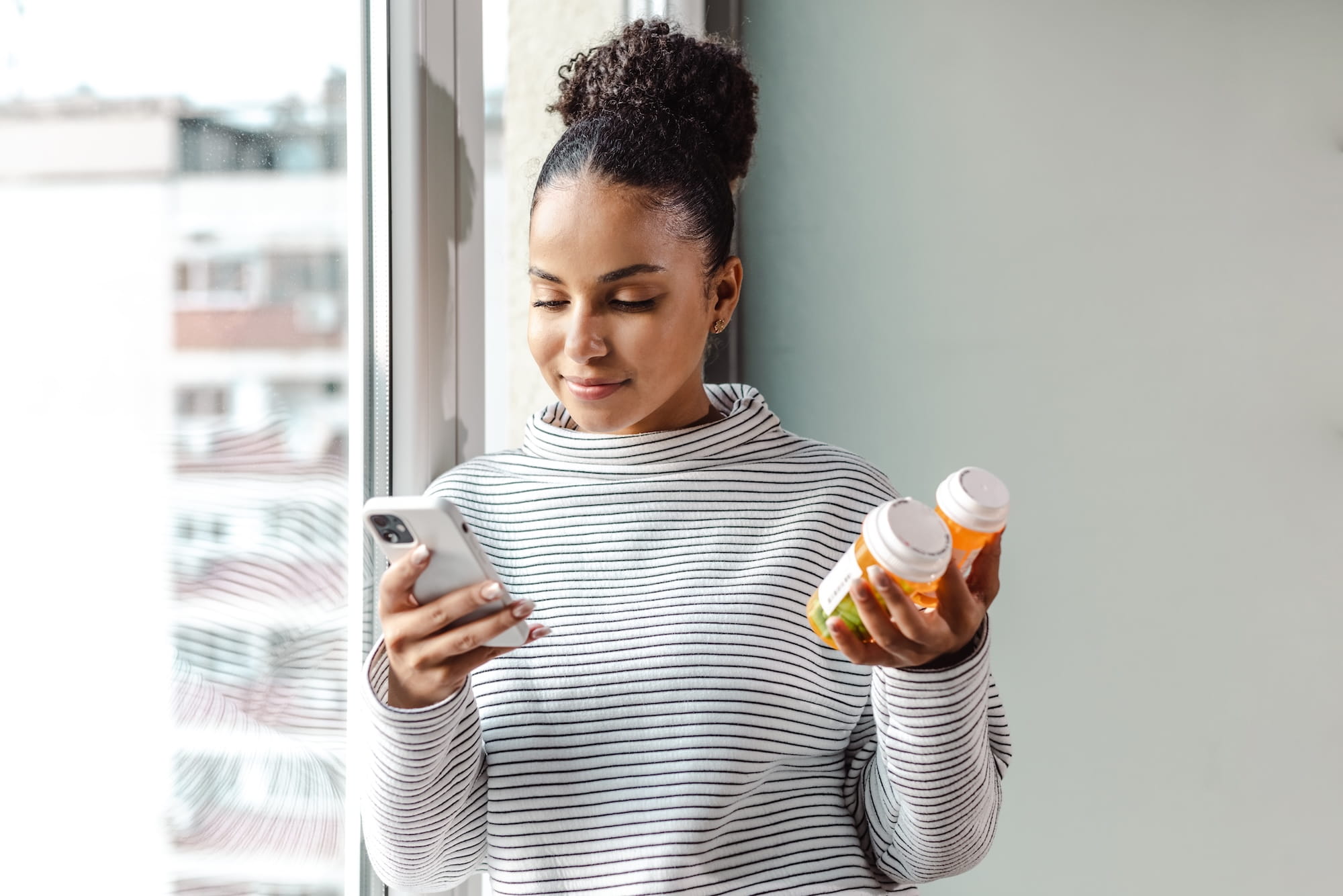 Woman looking at her phone while holding two prescription medication bottles