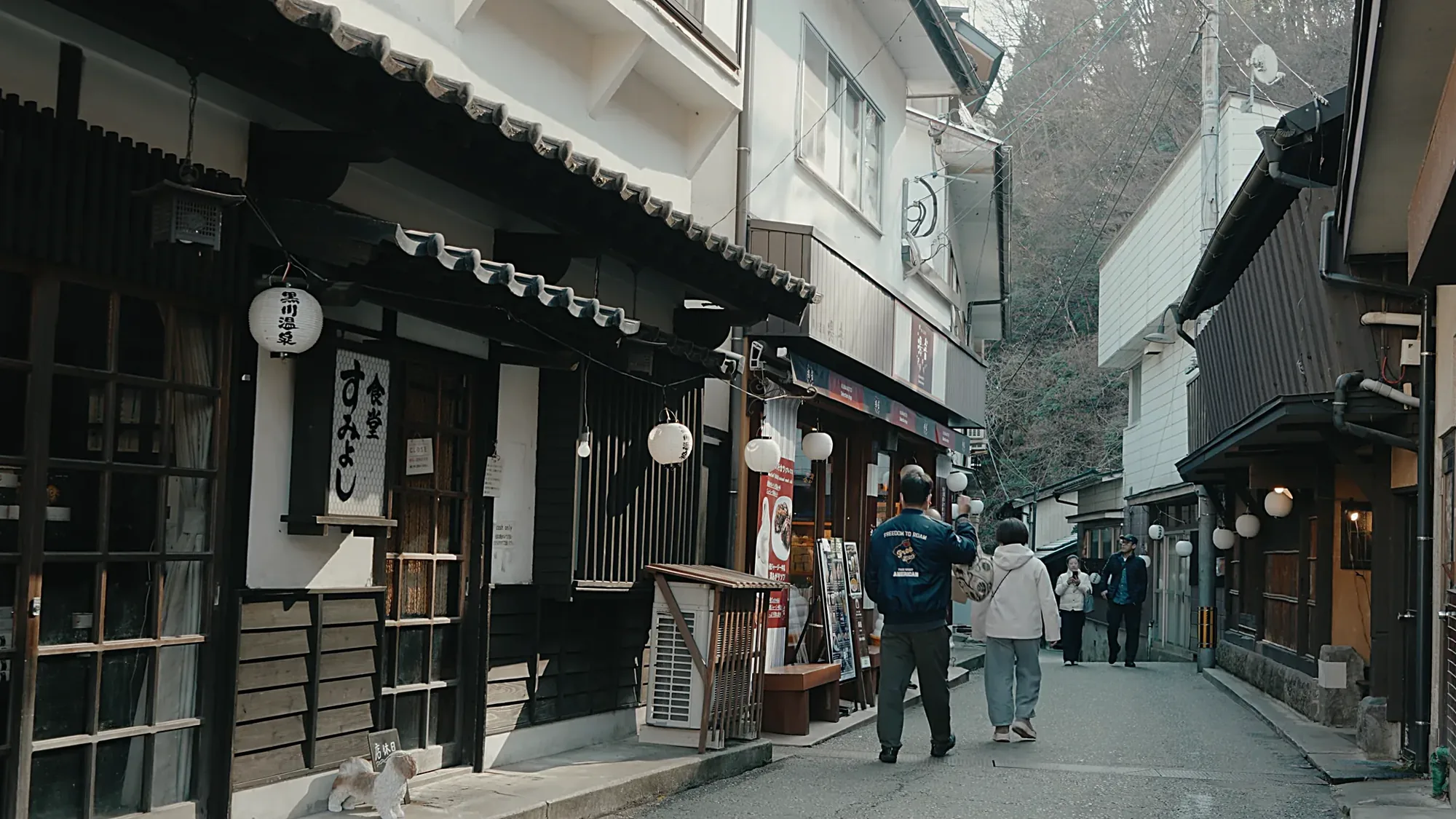 The main lane through Kurokawa Onsen, shopfronts and hanging lanterns, walkers in the street