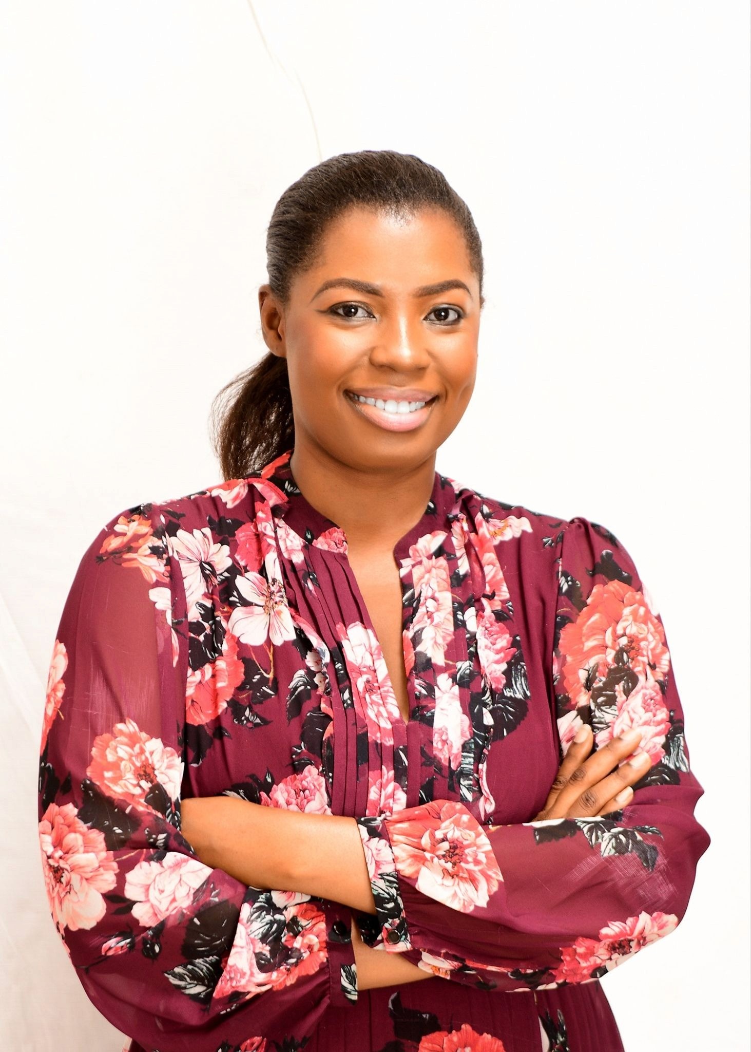 Abigail Owusu smiling with arms crossed in floral dress against white studio background.