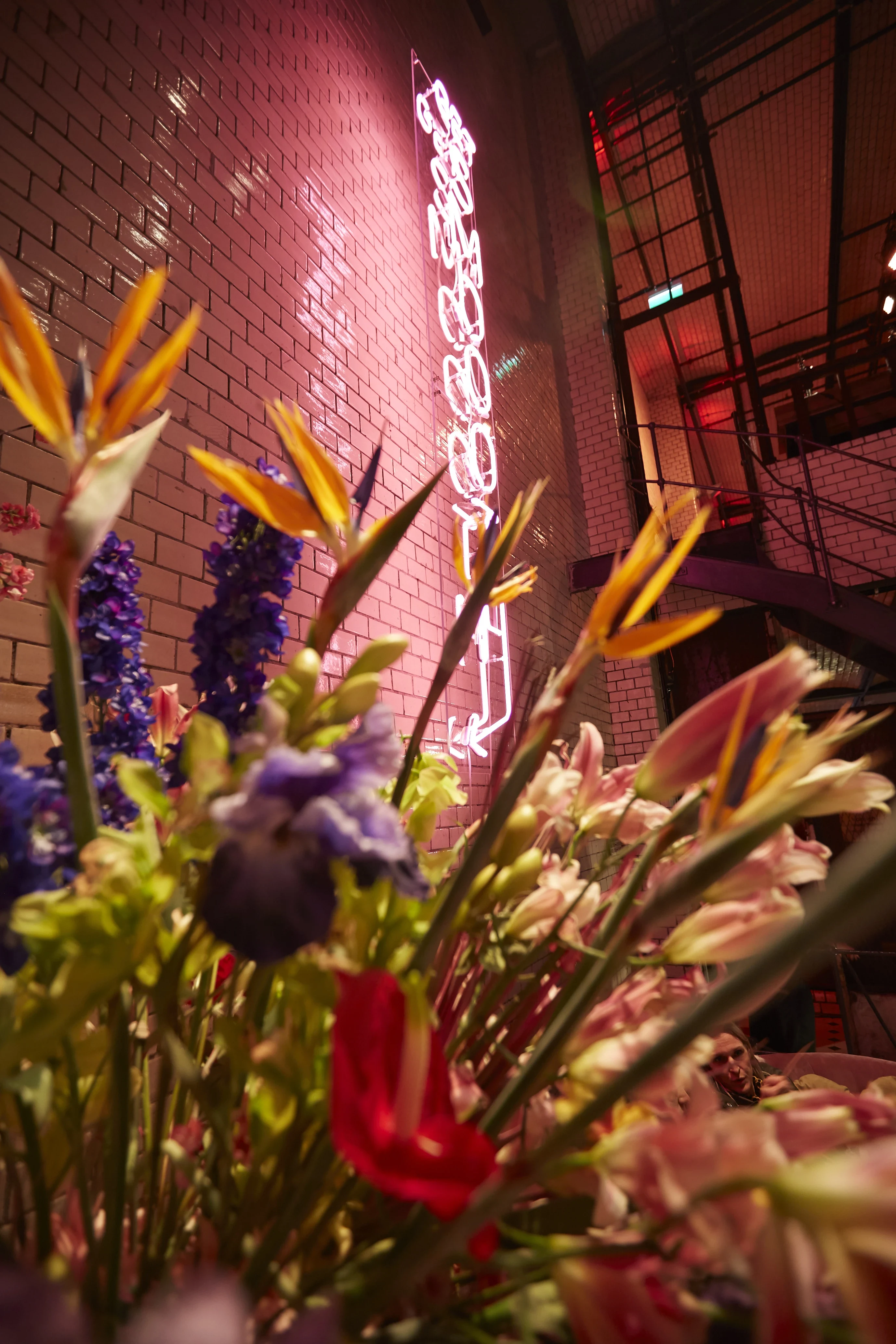 Pink Get Smoooth neon sign on a white tiled wall behind colorful flower arrangements at the Klarna Fashion Week pop-up.